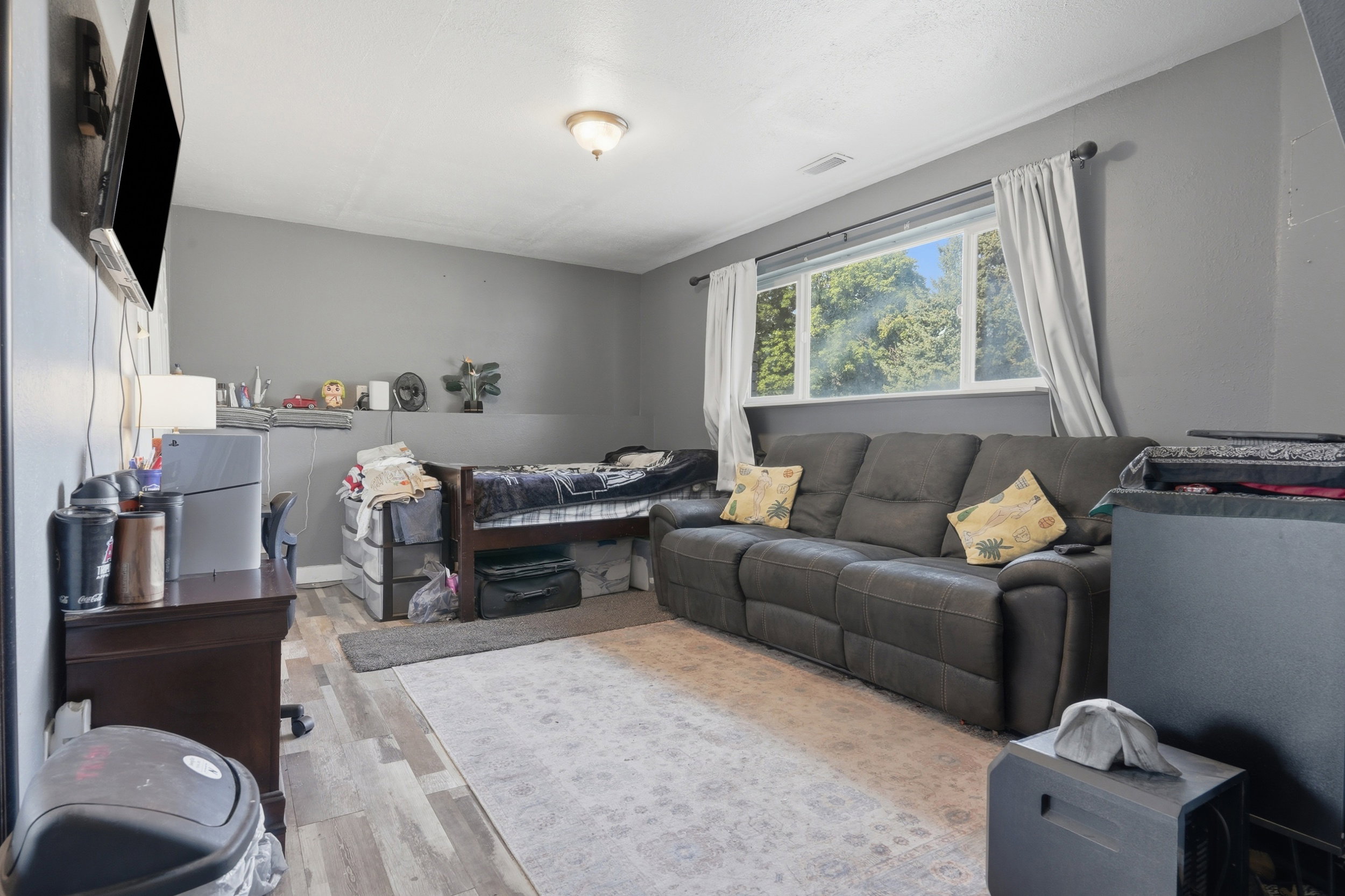 Spacious room featuring wood-finish flooring, a large window with exterior greenery, and neutral gray wall paint