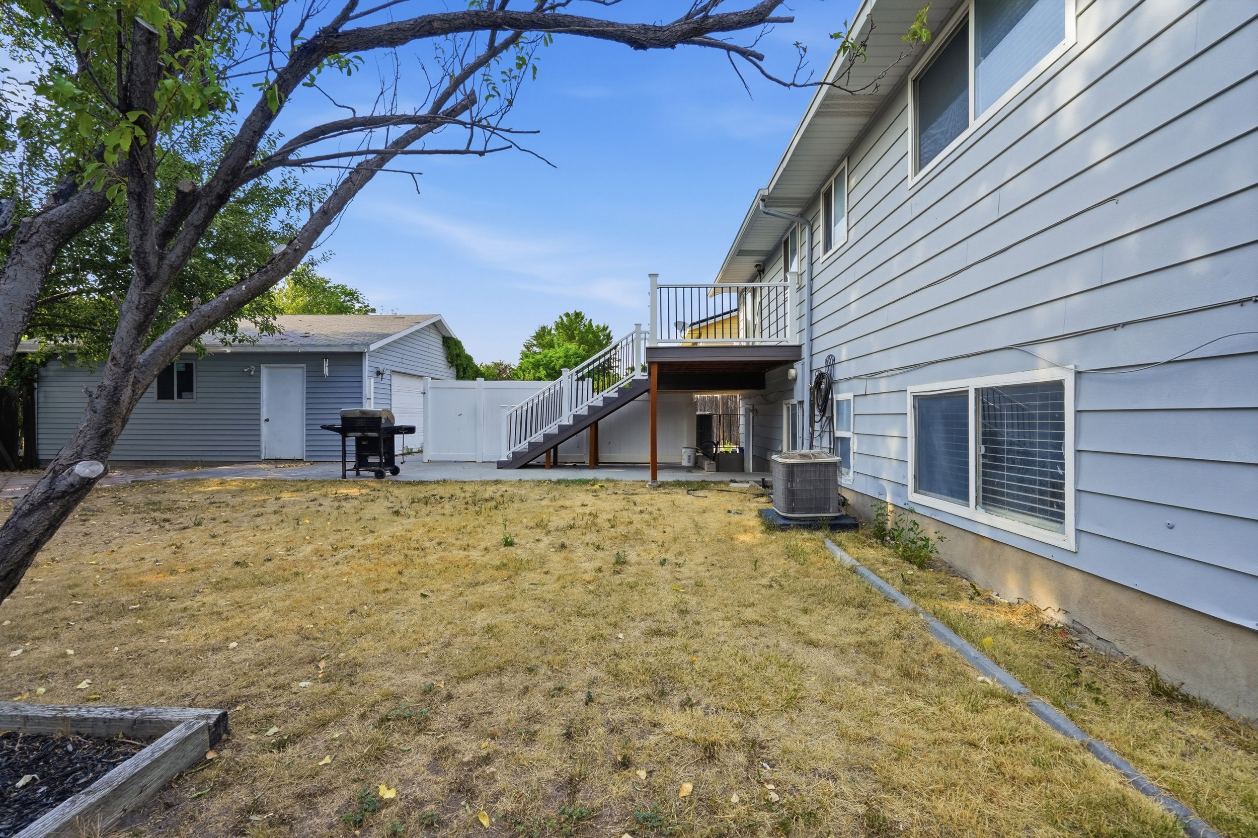 Rear exterior featuring a spacious deck with white railings, a detached garage, and a concrete patio
