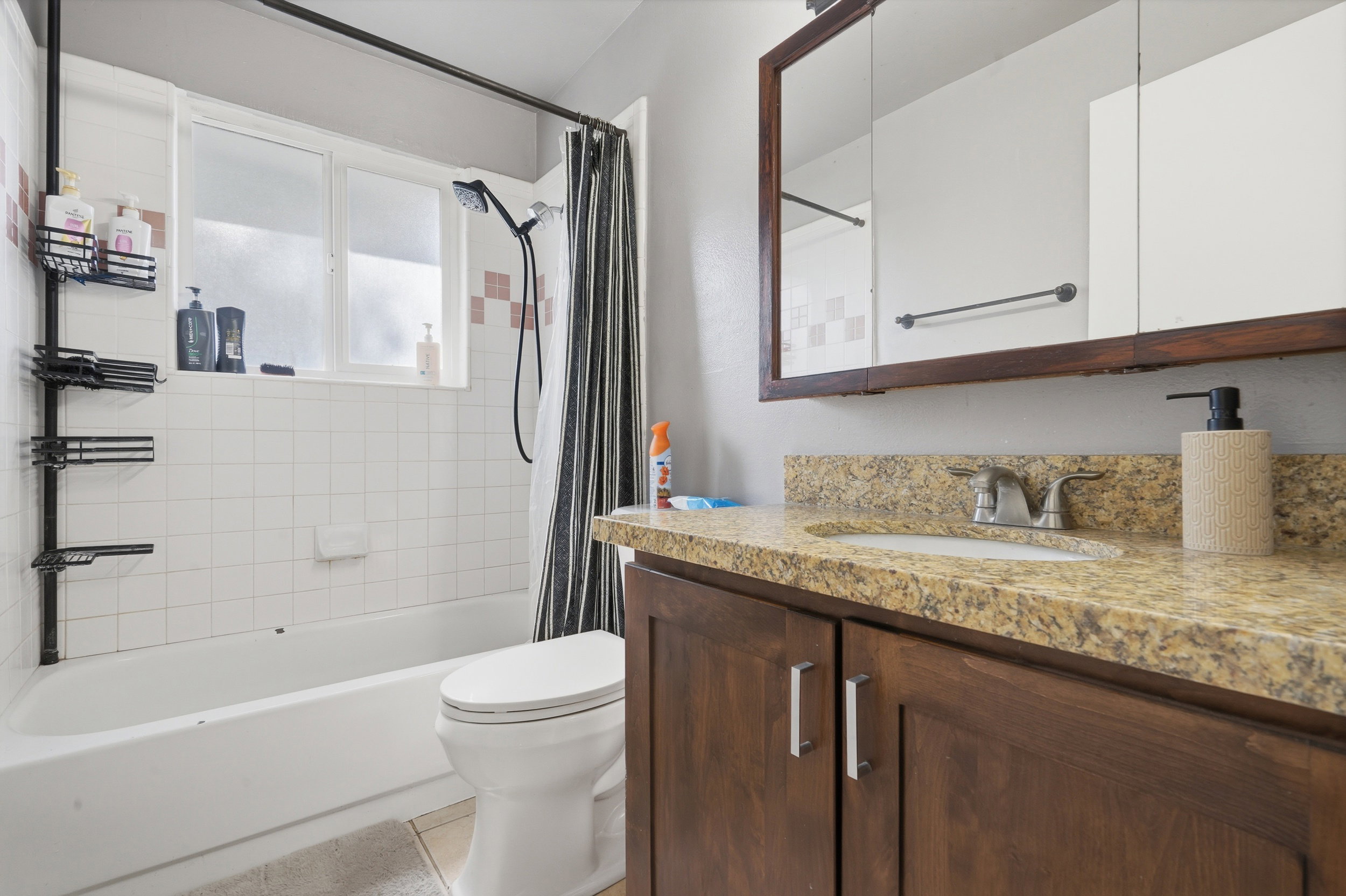 Bathroom featuring a white subway tile tub surround with an accent tile band, a vanity with wood-finish cabinetry, a granite-style countertop, and a medicine cabinet with a wood-finish frame