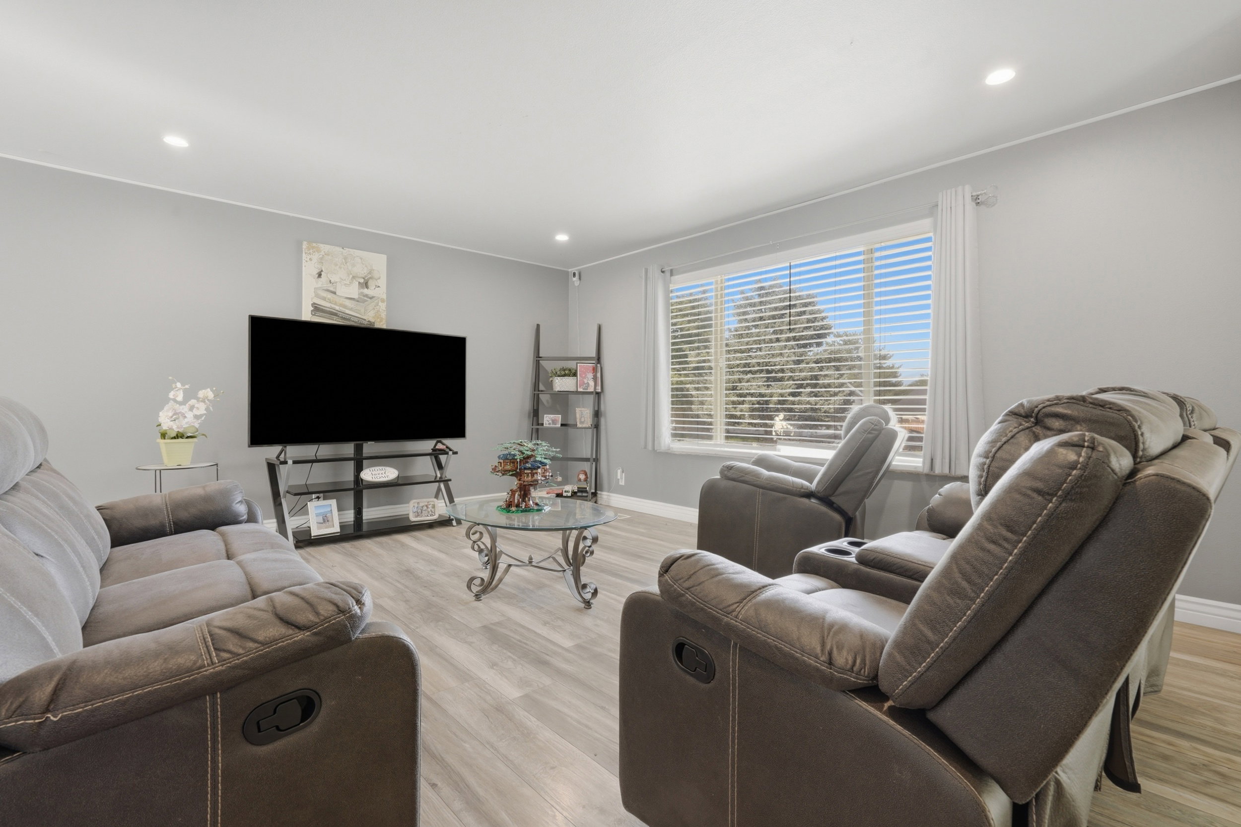 Spacious living area featuring light wood-finish flooring, a large window with blinds, recessed lighting, and light grey wall paint