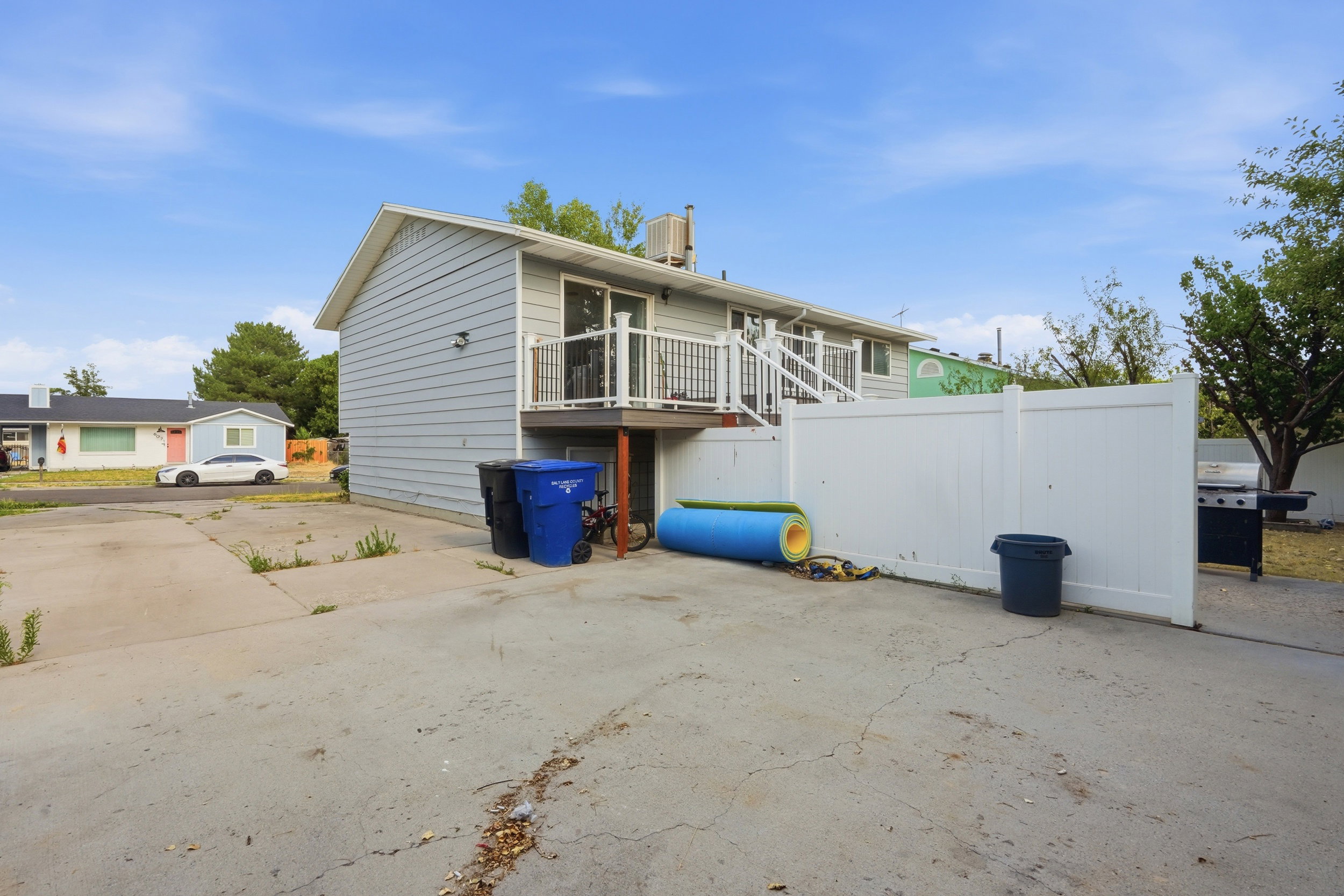 Rear exterior featuring light blue siding, an upper-level balcony with white railings, and a white privacy fence