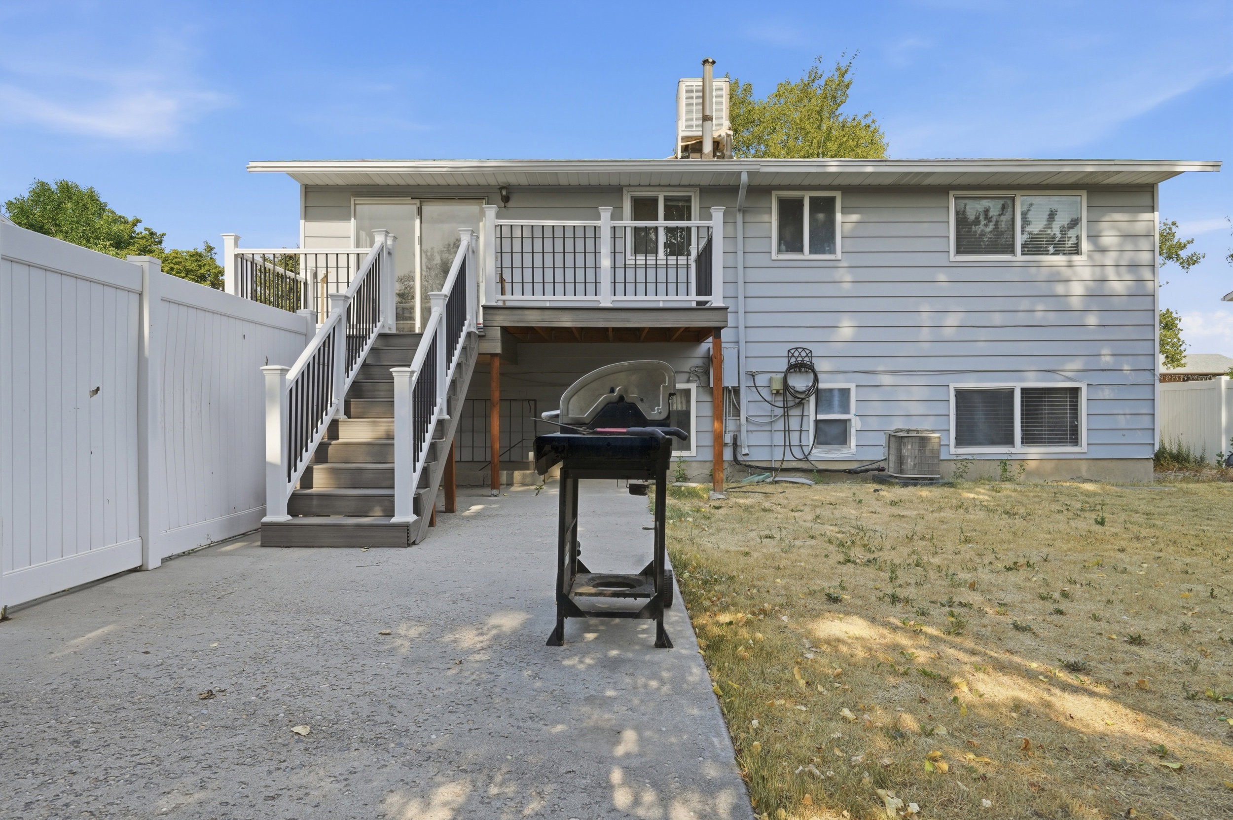 Rear exterior featuring light blue siding, a white privacy fence, a concrete patio, and an elevated deck with white and black railings