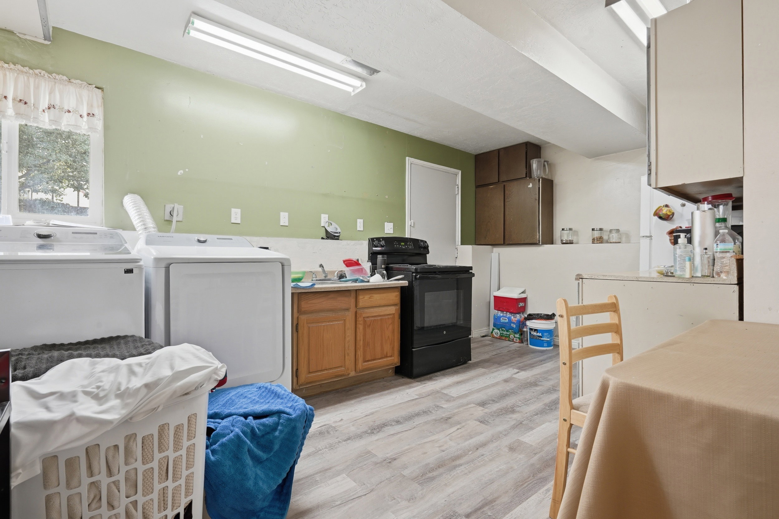 Utility area featuring wood-finish flooring, a window with natural light, integrated laundry hookups, built-in cabinetry, and a range appliance