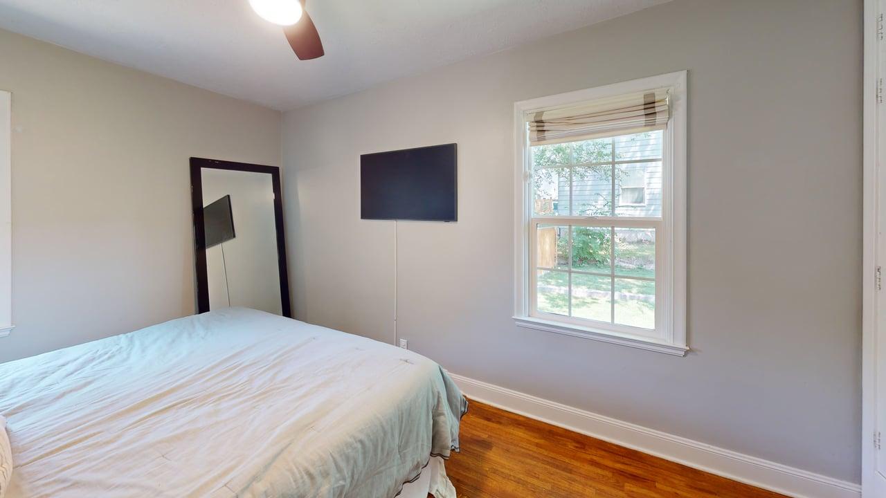 Bedroom with wood-finish flooring, a white-framed window, and a ceiling fan with light fixture