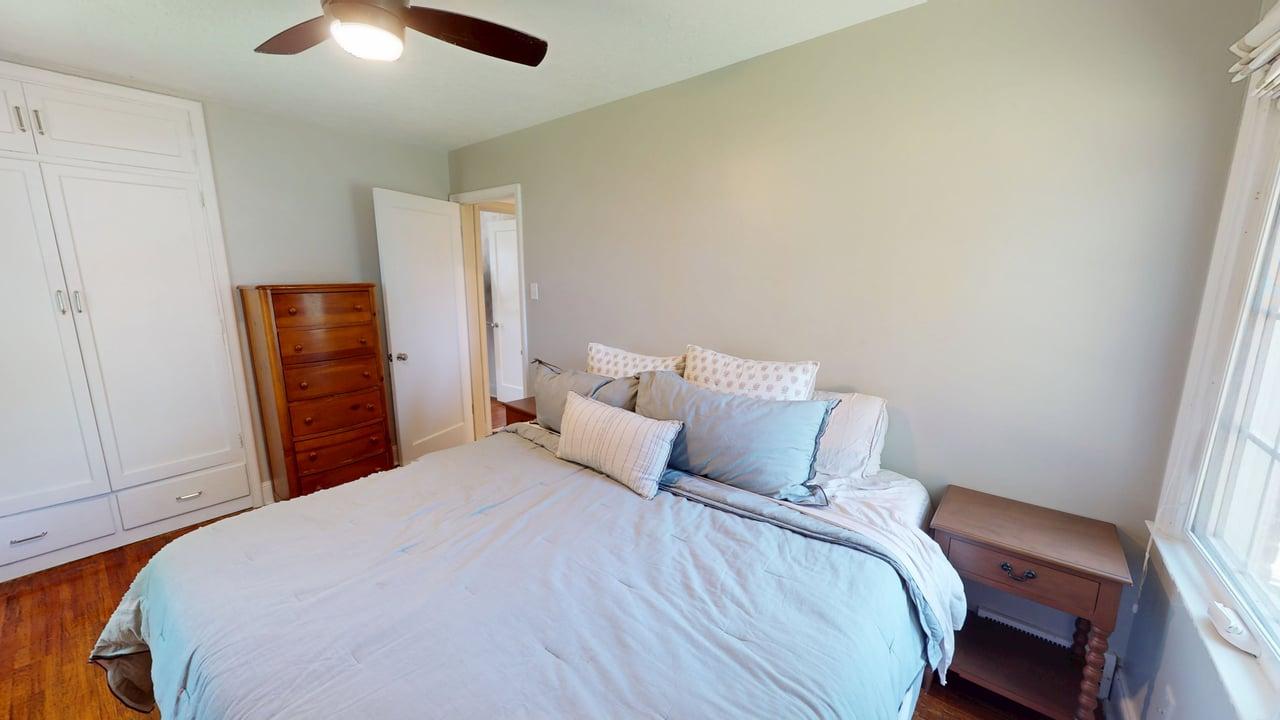 Bedroom featuring wood-finish flooring, a ceiling fan with integrated lighting, and white built-in cabinetry