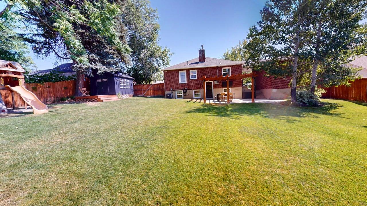 Expansive green lawn featuring a red brick exterior, a wood pergola over a patio, a detached shed with a wood deck, and mature trees