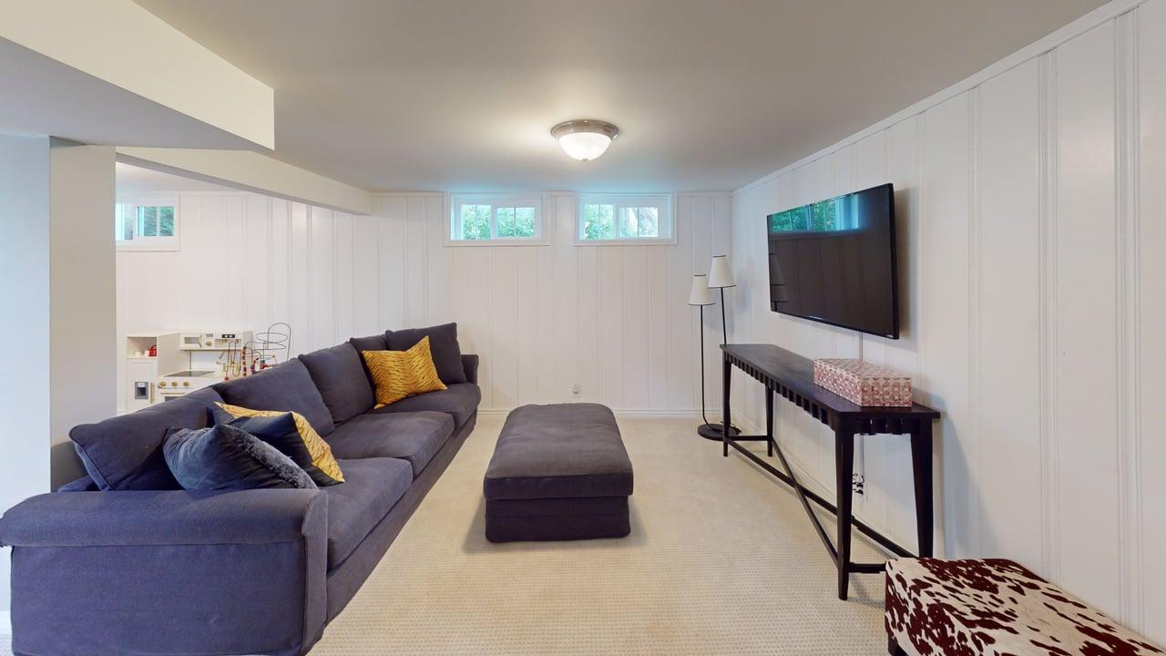 Spacious lower-level living area featuring white paneled walls and light-toned carpet