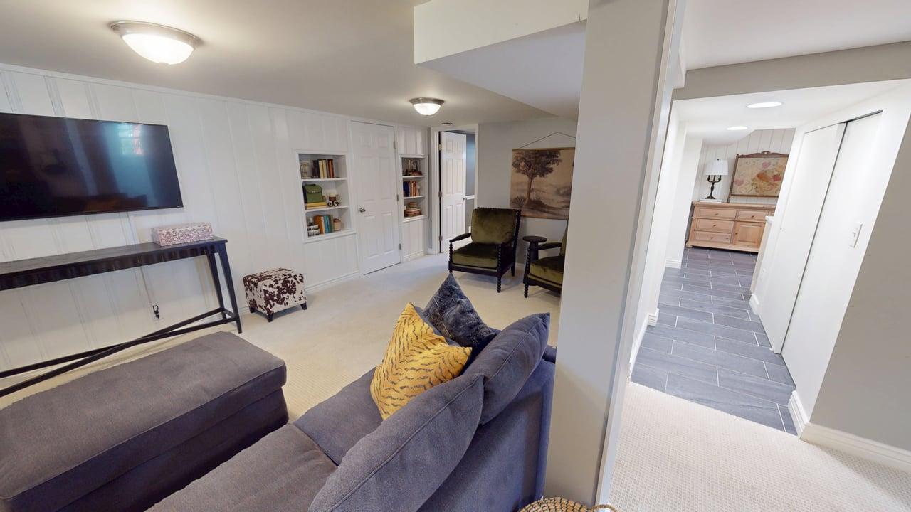 Finished lower level featuring recessed built-in shelving, white paneled walls, and soft neutral carpeting