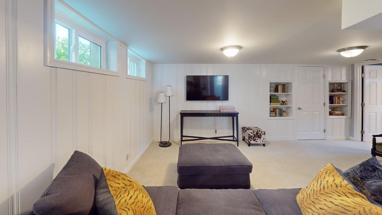 Finished lower level featuring recessed windows, white beadboard paneling, built-in shelving, mounted television, and carpeted flooring