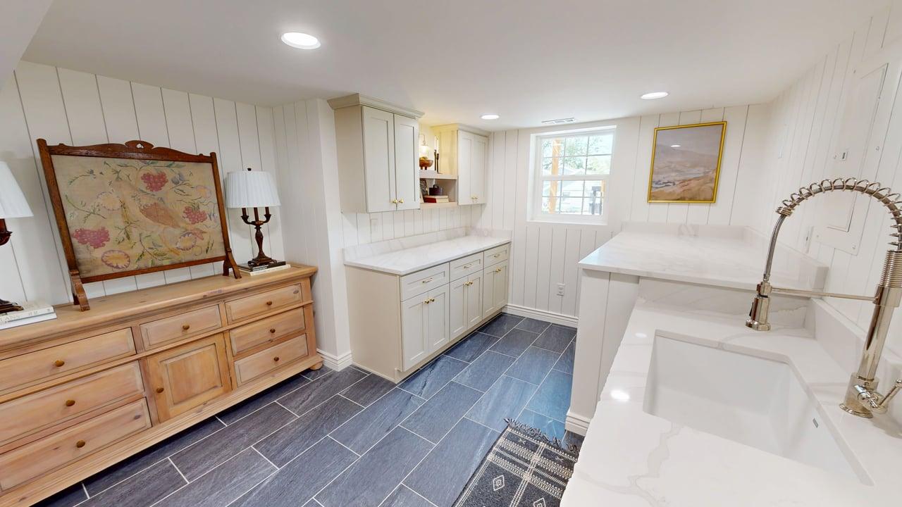 Utility room featuring a built-in sink with a gooseneck faucet, light-toned cabinetry, solid surface countertops, white vertical paneling, and dark rectangular floor tiling