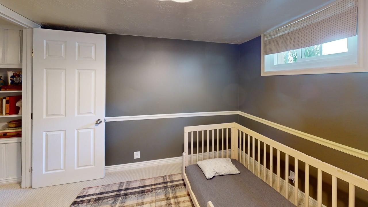 Carpeted room with a white six-panel door, built-in shelving, a window with a roller shade, and two-tone walls with chair rail molding