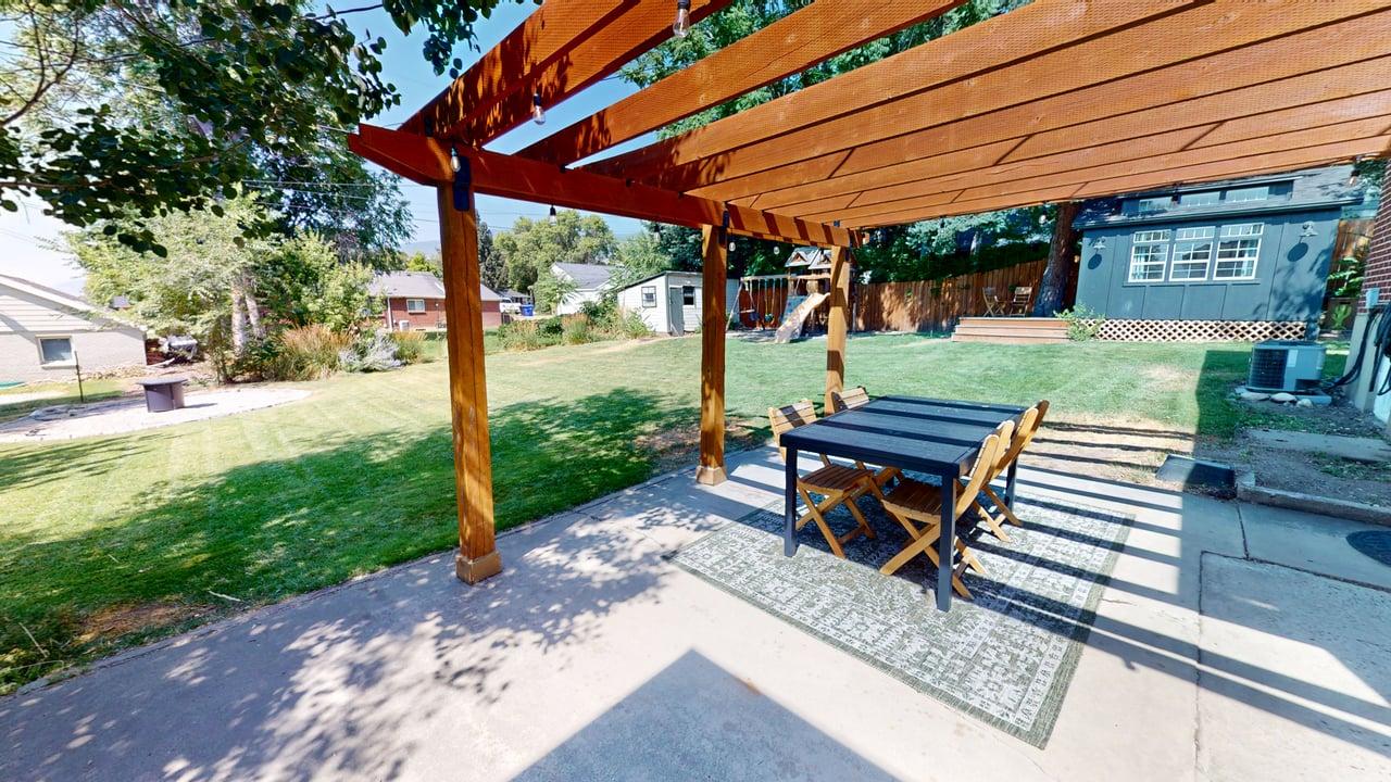 Expansive backyard featuring a concrete patio with a wooden pergola structure, a large grassy area, a detached storage shed, and mature trees
