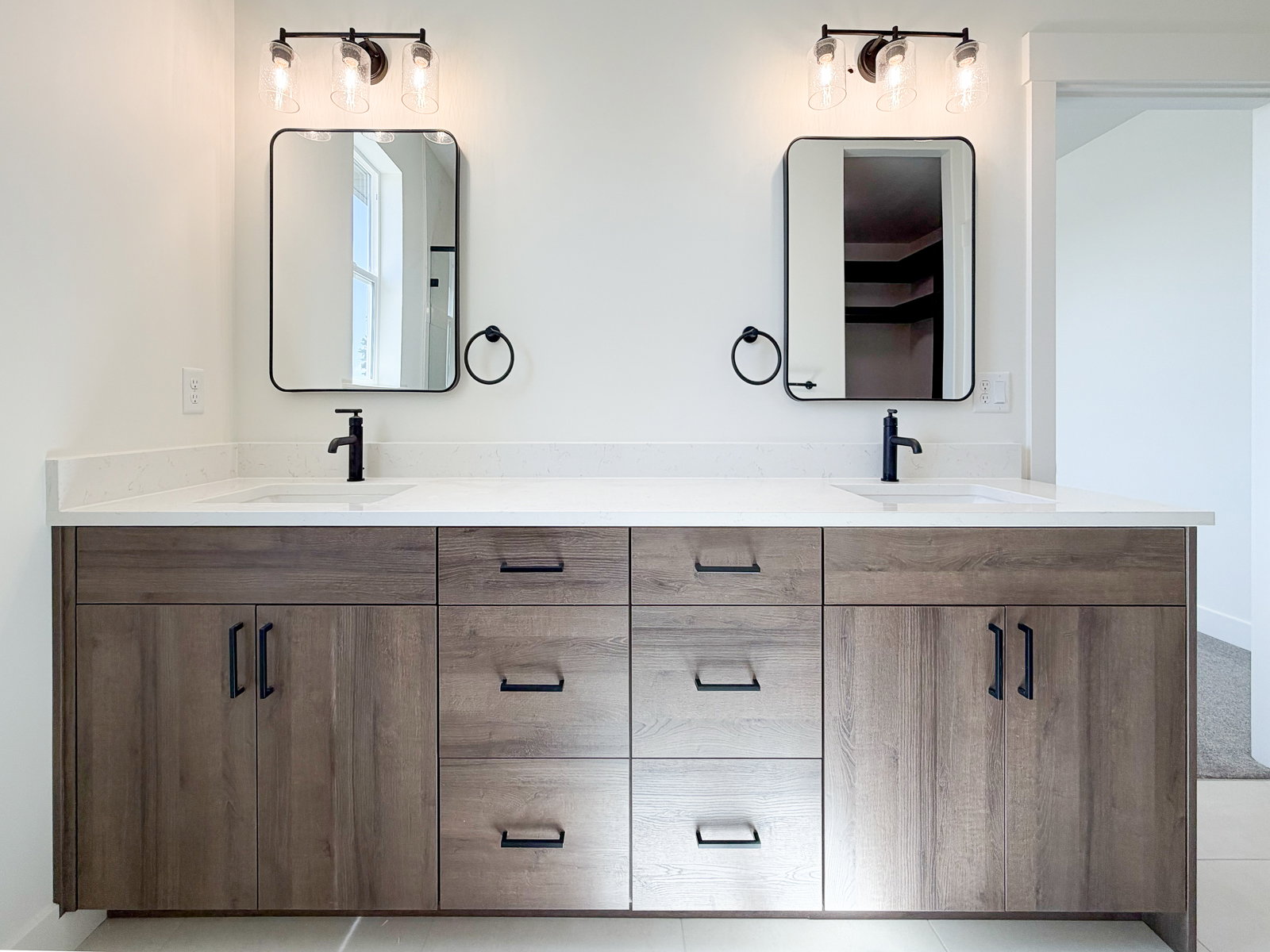 Double vanity featuring wood-finish cabinetry with matte black hardware, white countertops, and integrated rectangular sinks