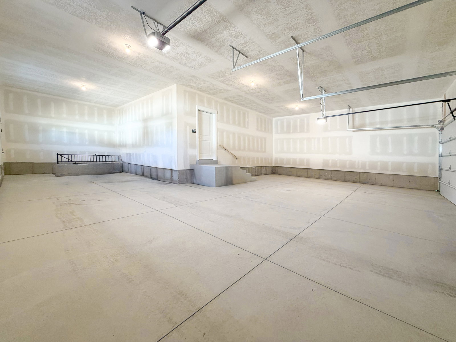 Spacious garage featuring a concrete floor, high ceilings, exposed drywall, and overhead lighting