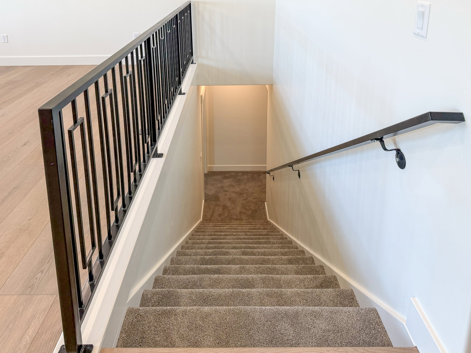 Staircase featuring dark carpeted steps, a black metal handrail, and a black metal baluster with geometric accents