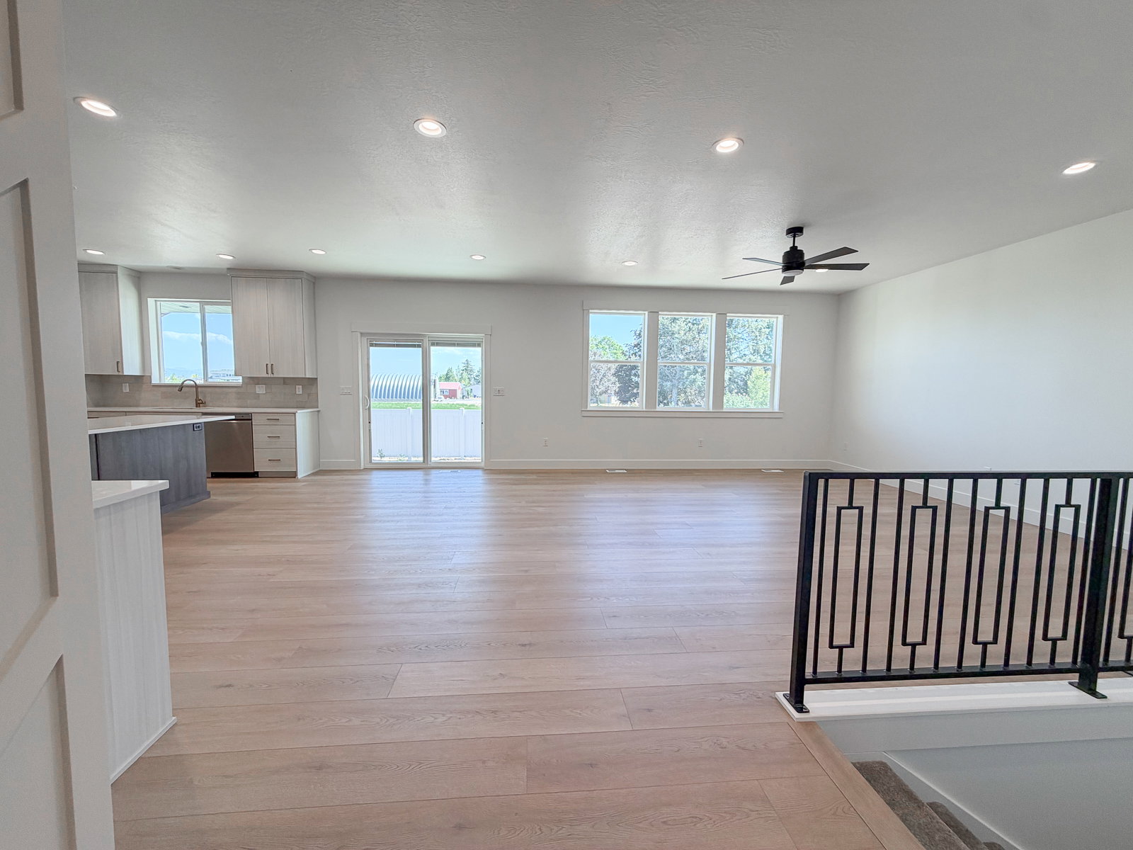 Spacious open-concept living area featuring light wood-finish flooring, recessed lighting, and a modern ceiling fan