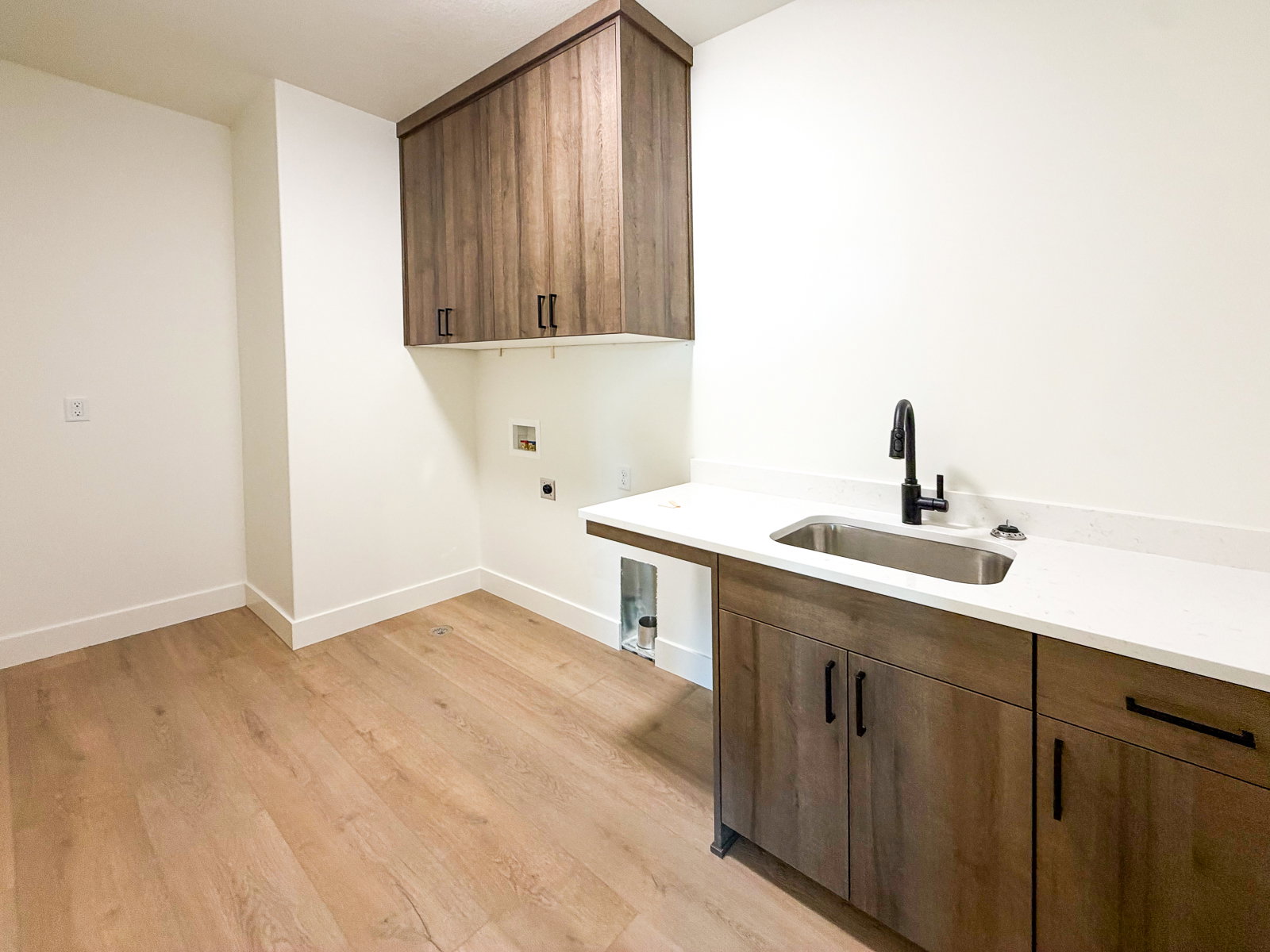Laundry room featuring wood-finish flooring, white walls, and built-in cabinetry