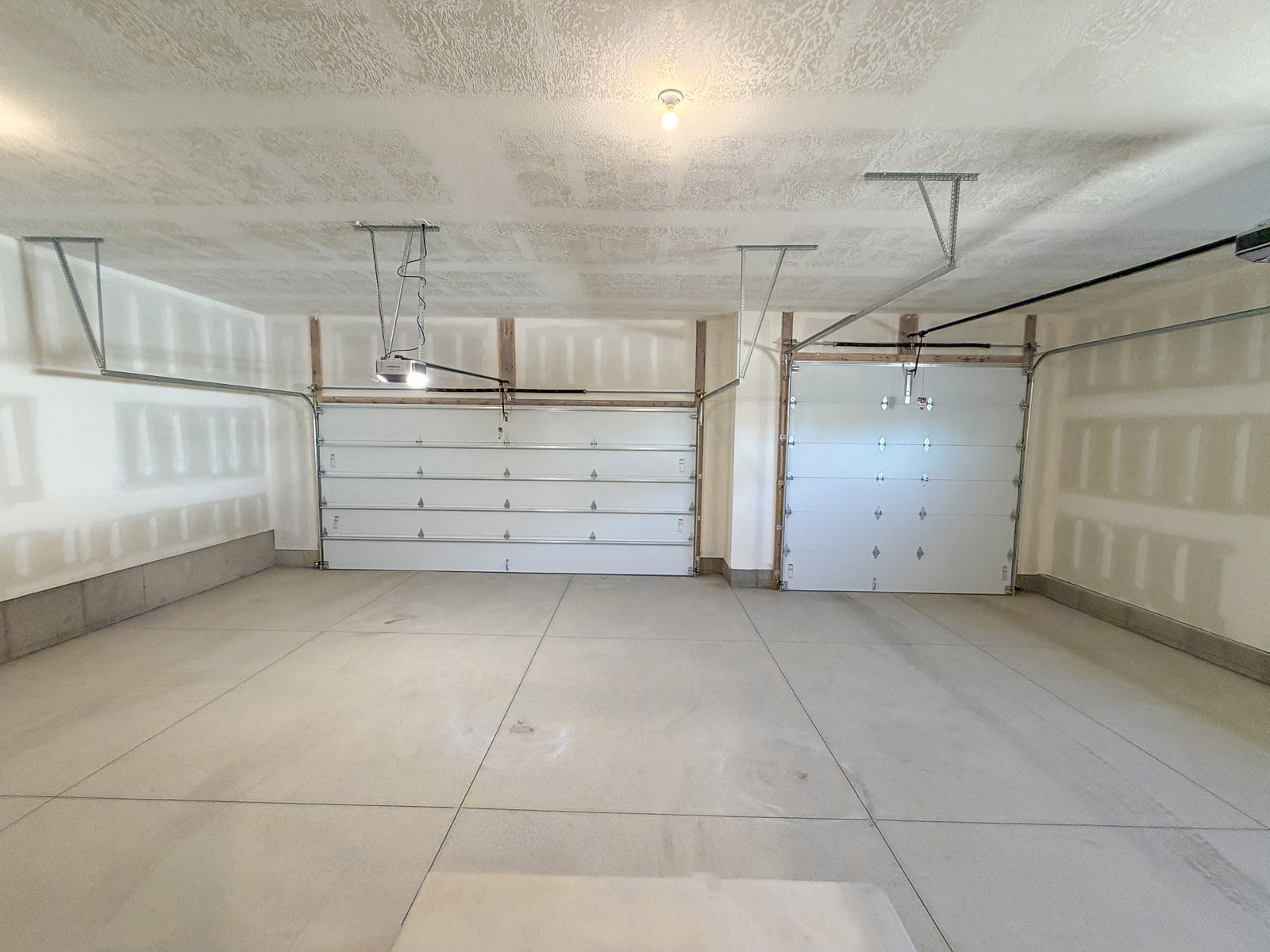 Spacious two-car garage featuring concrete flooring, two overhead garage doors with automatic openers, and exposed framing