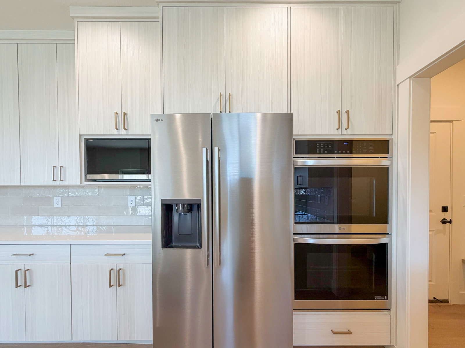 Stainless steel side-by-side refrigerator, built-in microwave, and double wall ovens complement the light-toned cabinetry with brass hardware