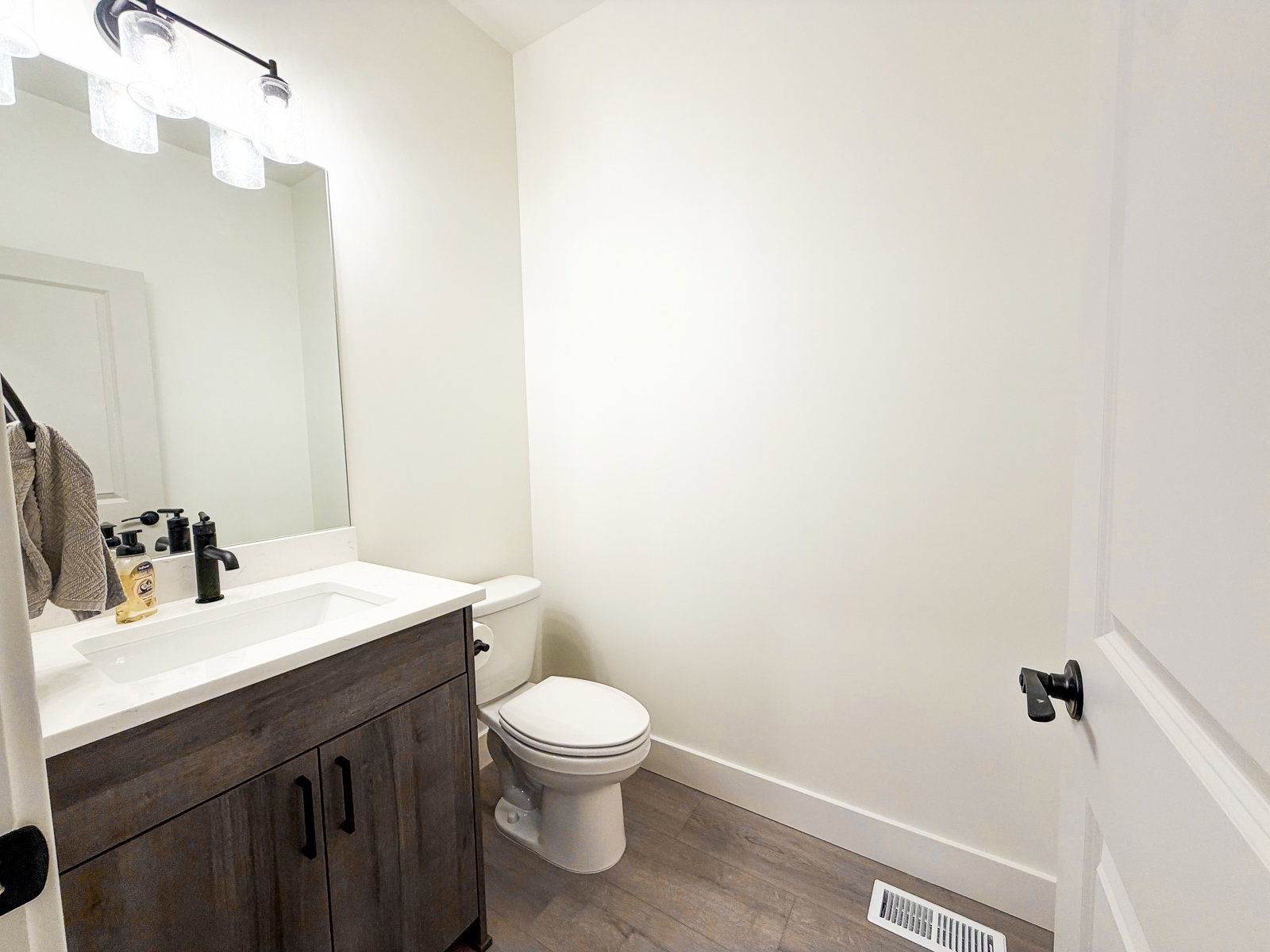 Bathroom featuring a wood-finish vanity with a white countertop and integrated sink, a contemporary matte black faucet, and a wall-mounted light fixture with frosted glass shades