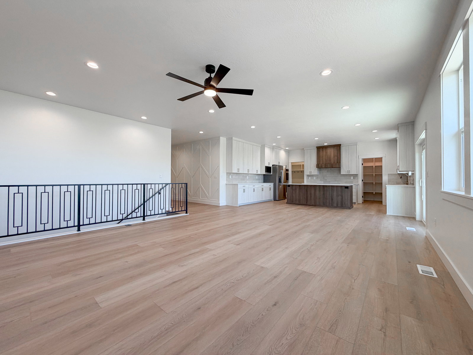 Spacious open-concept interior featuring light wood-finish flooring, recessed lighting, and a modern ceiling fan