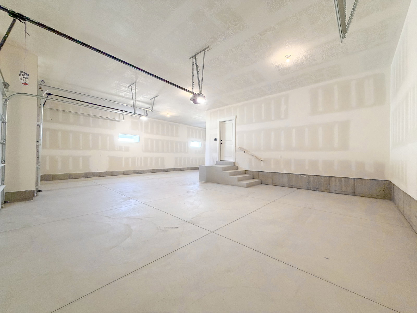 Spacious garage featuring concrete flooring, unpainted drywall, and exposed ceiling joists