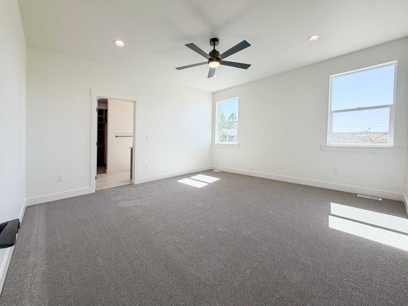 Spacious room featuring gray carpeting, multiple windows, recessed lighting, and a ceiling fan with a dark finish