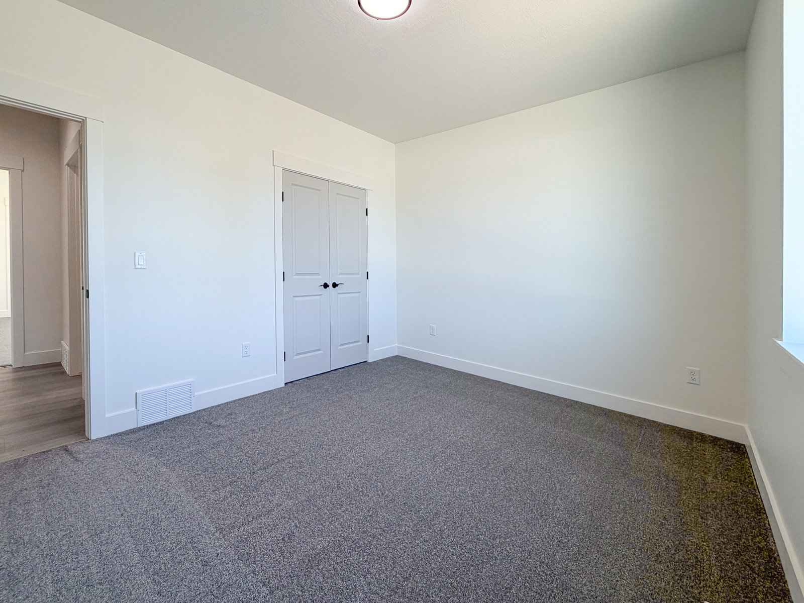 Neutral-toned room featuring a window, light gray carpeting, crisp white walls, and a closet with double doors