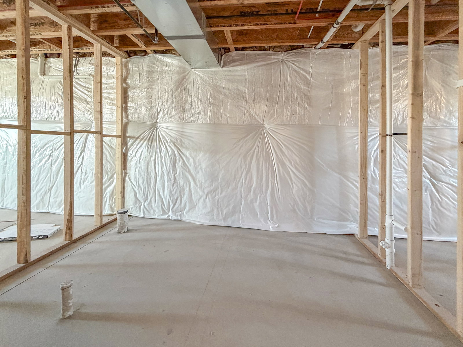Unfinished basement space featuring exposed wood framing, concrete flooring, and insulated walls