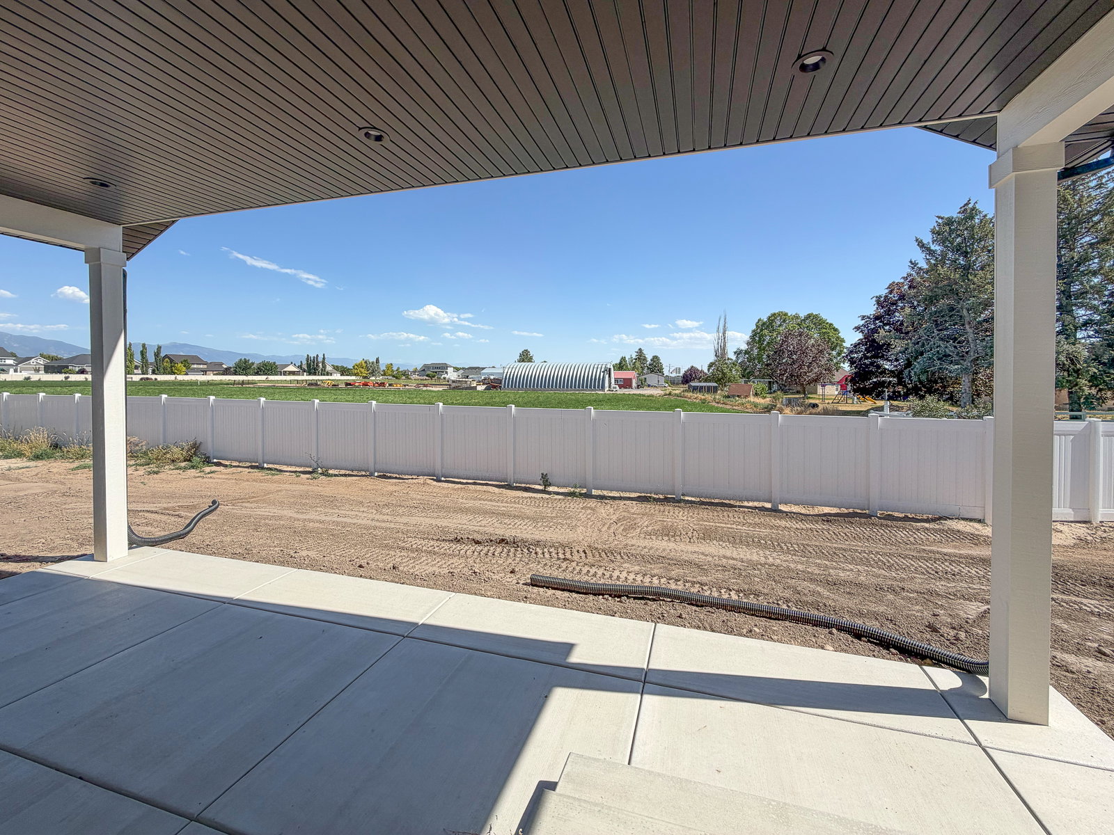 Covered concrete patio with recessed lighting, white vinyl privacy fencing, and expansive field beyond