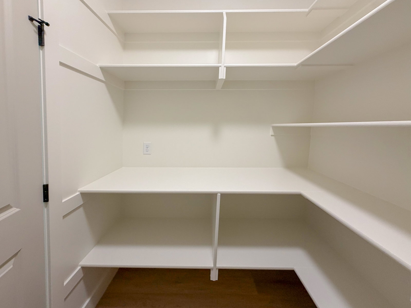 Walk-in pantry featuring white shelving, a power outlet, and wood-finish flooring