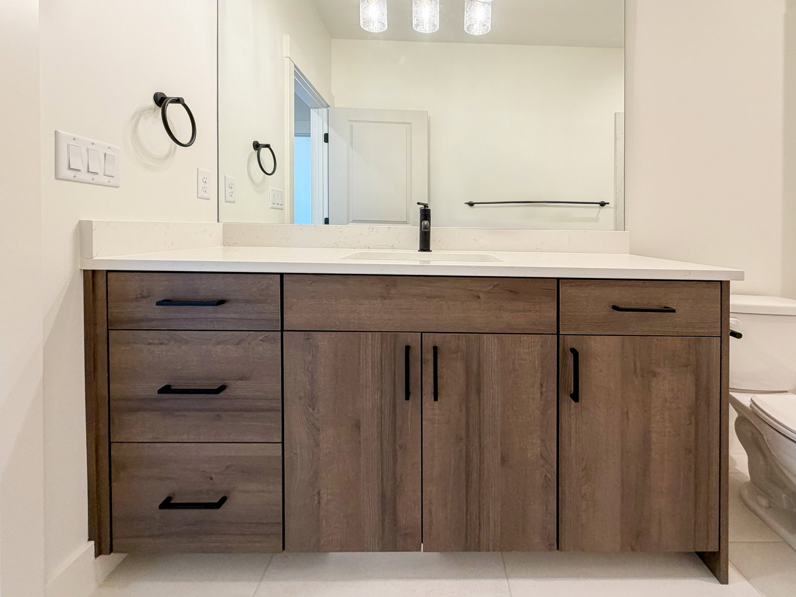Floating vanity with wood-finish cabinetry and black hardware, featuring a white countertop and integrated sink