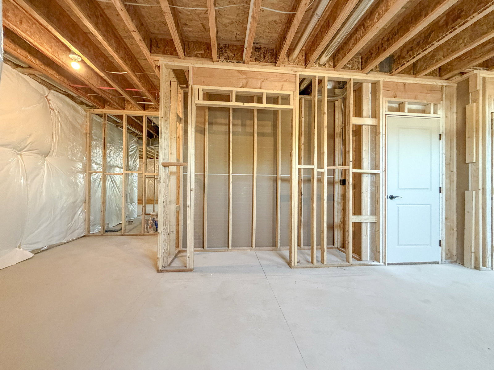 Unfinished basement featuring exposed wood framing, white vapor barrier, and a concrete floor