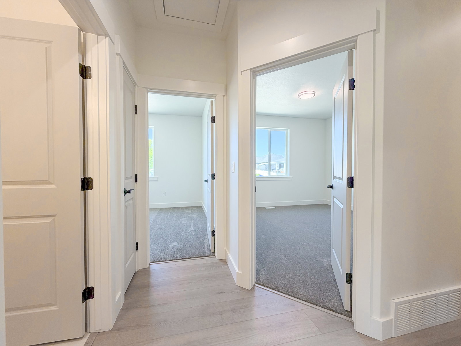 Hallway featuring light wood-finish flooring, white paneled doors with black hardware, and crisp white trimwork