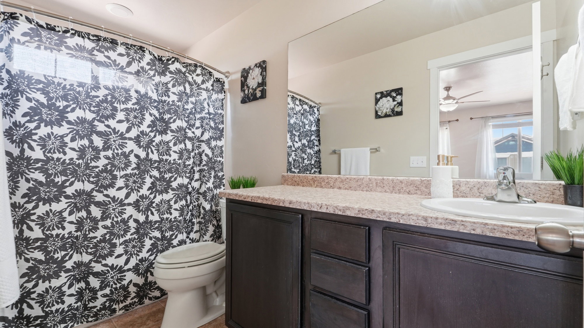 Bathroom featuring a dark wood-finish vanity with a single basin sink, a large wall-mounted mirror, and a shower-over-tub combination with a window