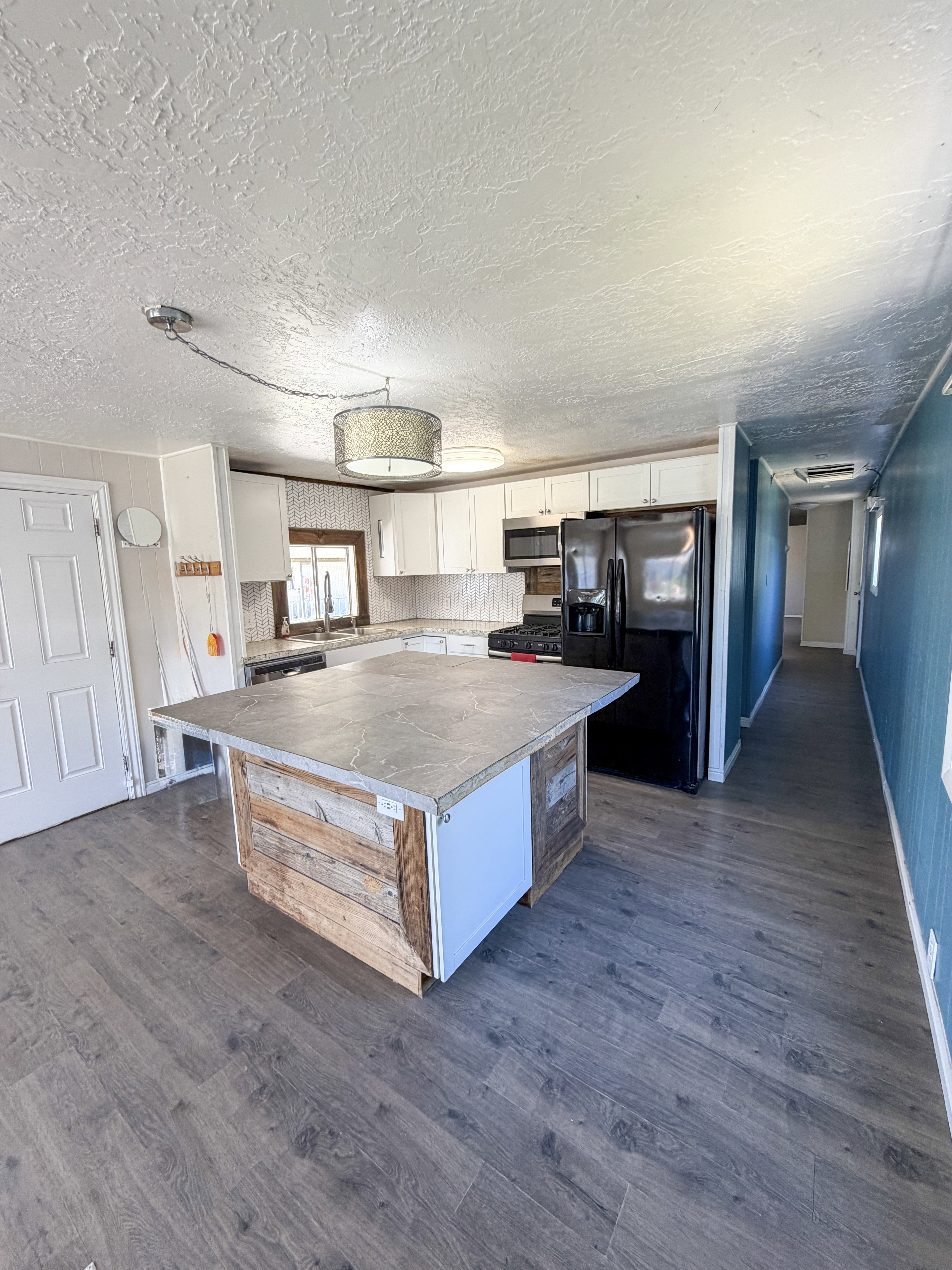 Kitchen featuring a central island with wood-finish paneling and solid surface countertop, white cabinetry with modern hardware, stainless steel appliances, and wood-finish flooring