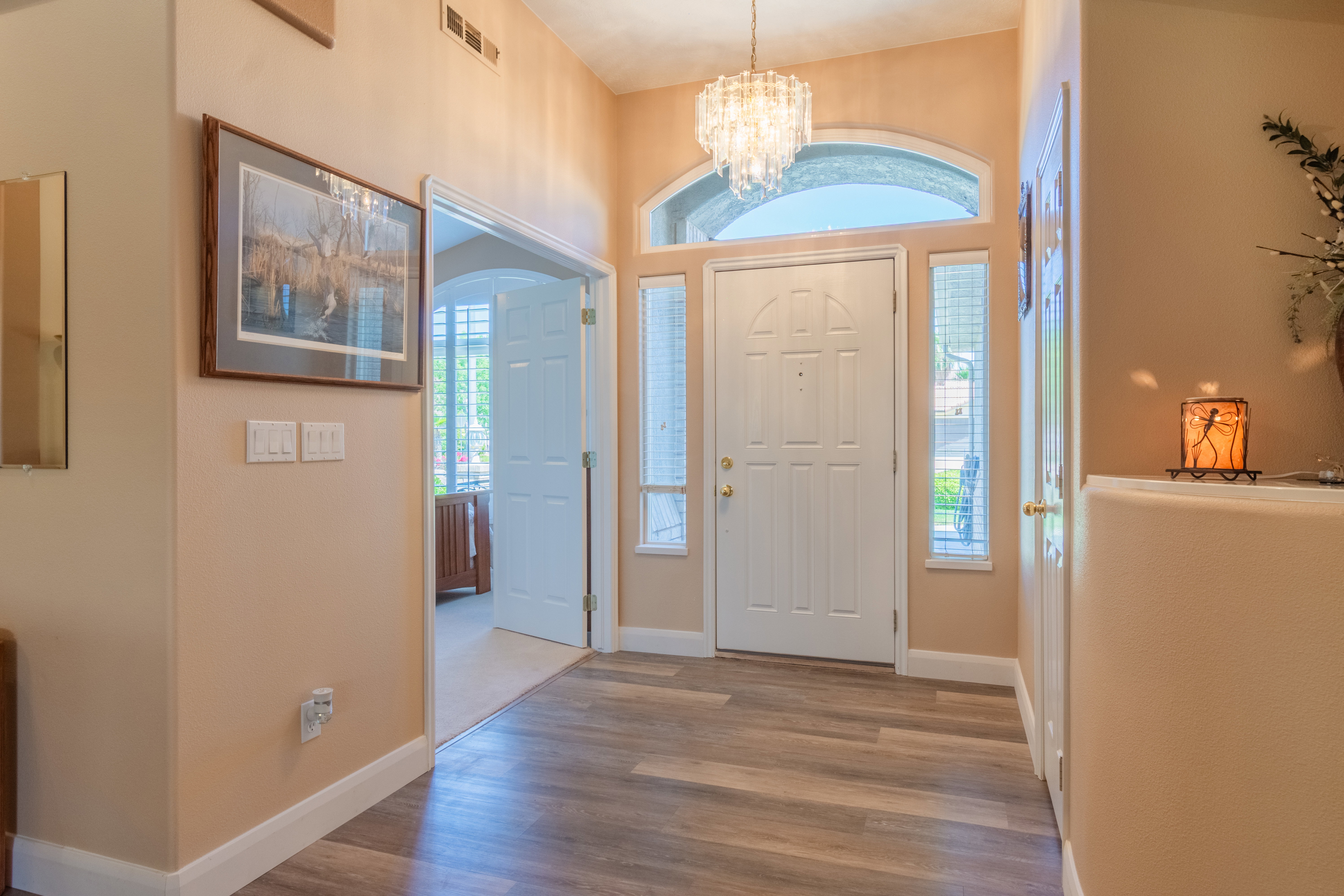 Foyer featuring wood-finish flooring, a white paneled entry door with sidelights and an arched transom, and a crystal chandelier