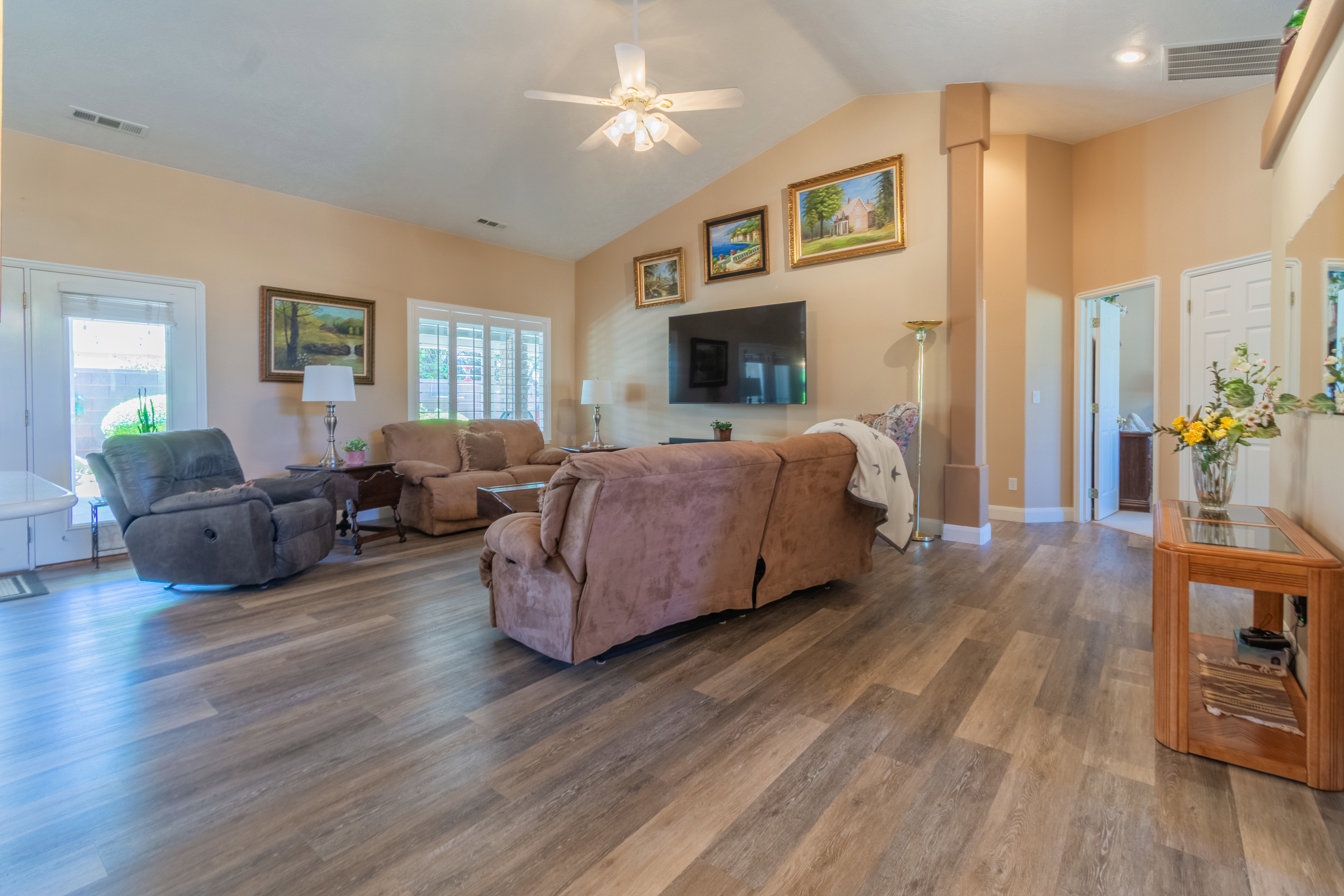Spacious living area featuring vaulted ceilings, wood-finish flooring, a ceiling fan, and ample natural light from multiple windows