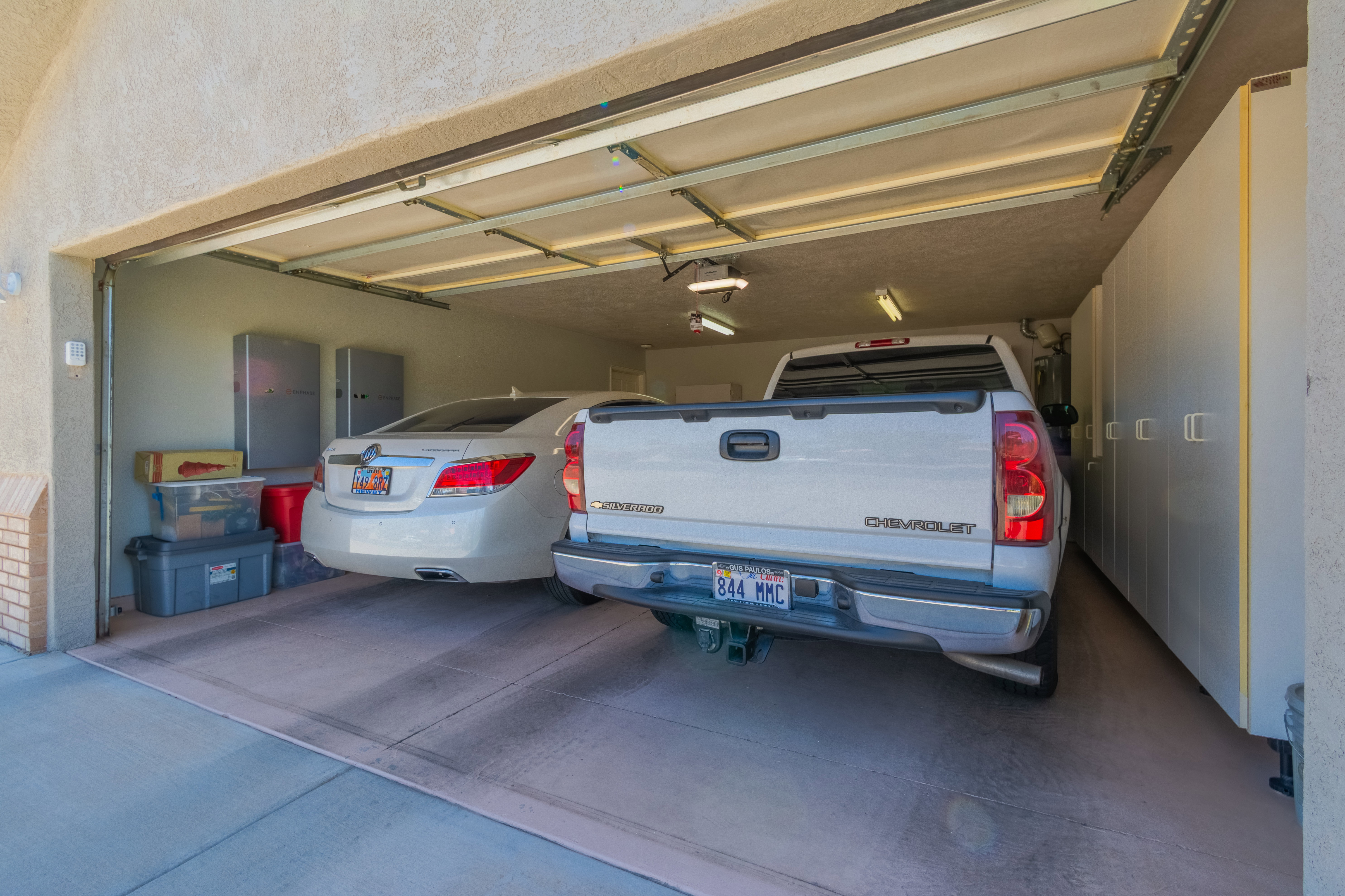 Spacious two-car garage featuring a textured concrete floor, overhead fluorescent lighting, and extensive built-in cabinetry along one wall
