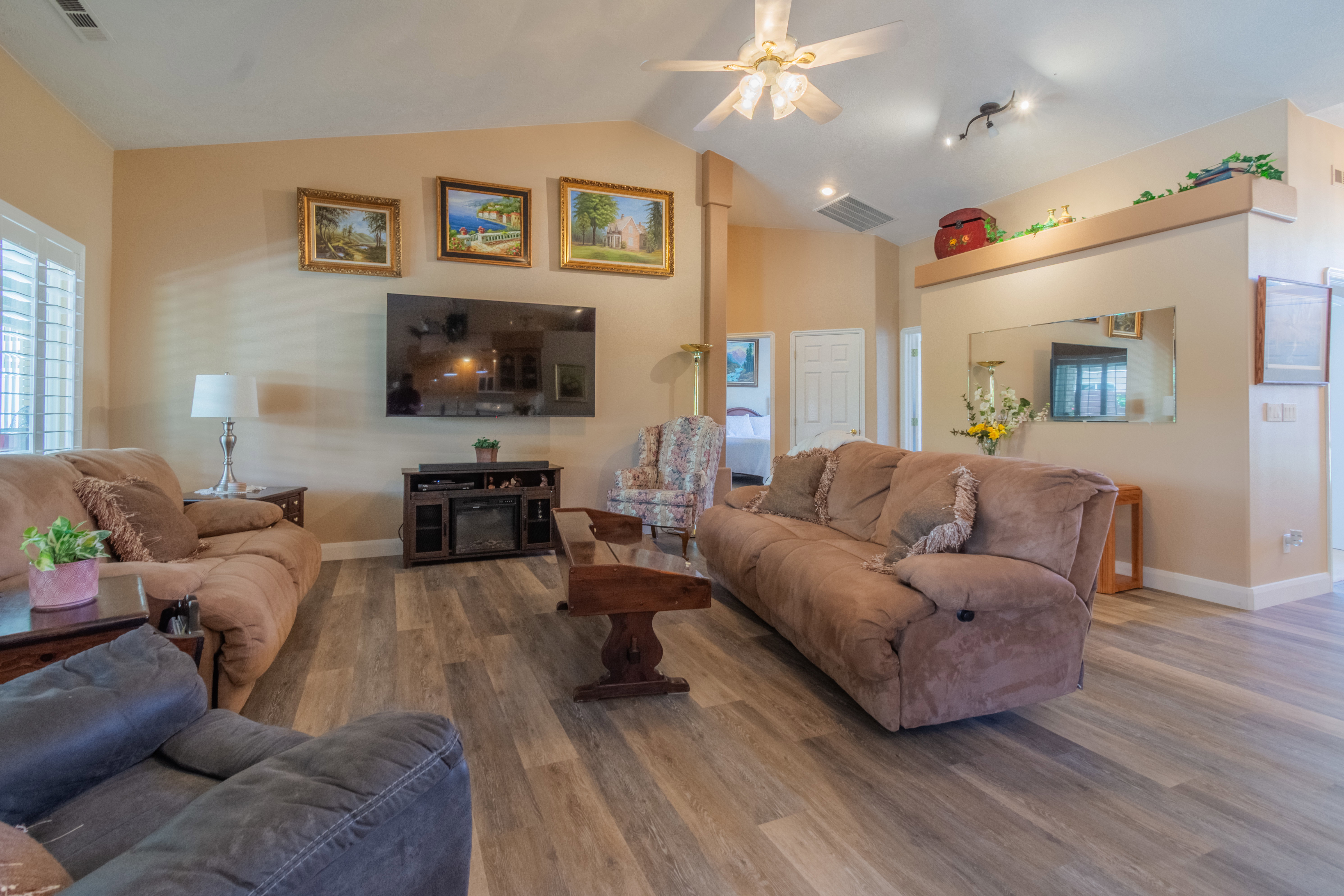 Spacious living area featuring wood-finish flooring, vaulted ceilings, and a ceiling fan