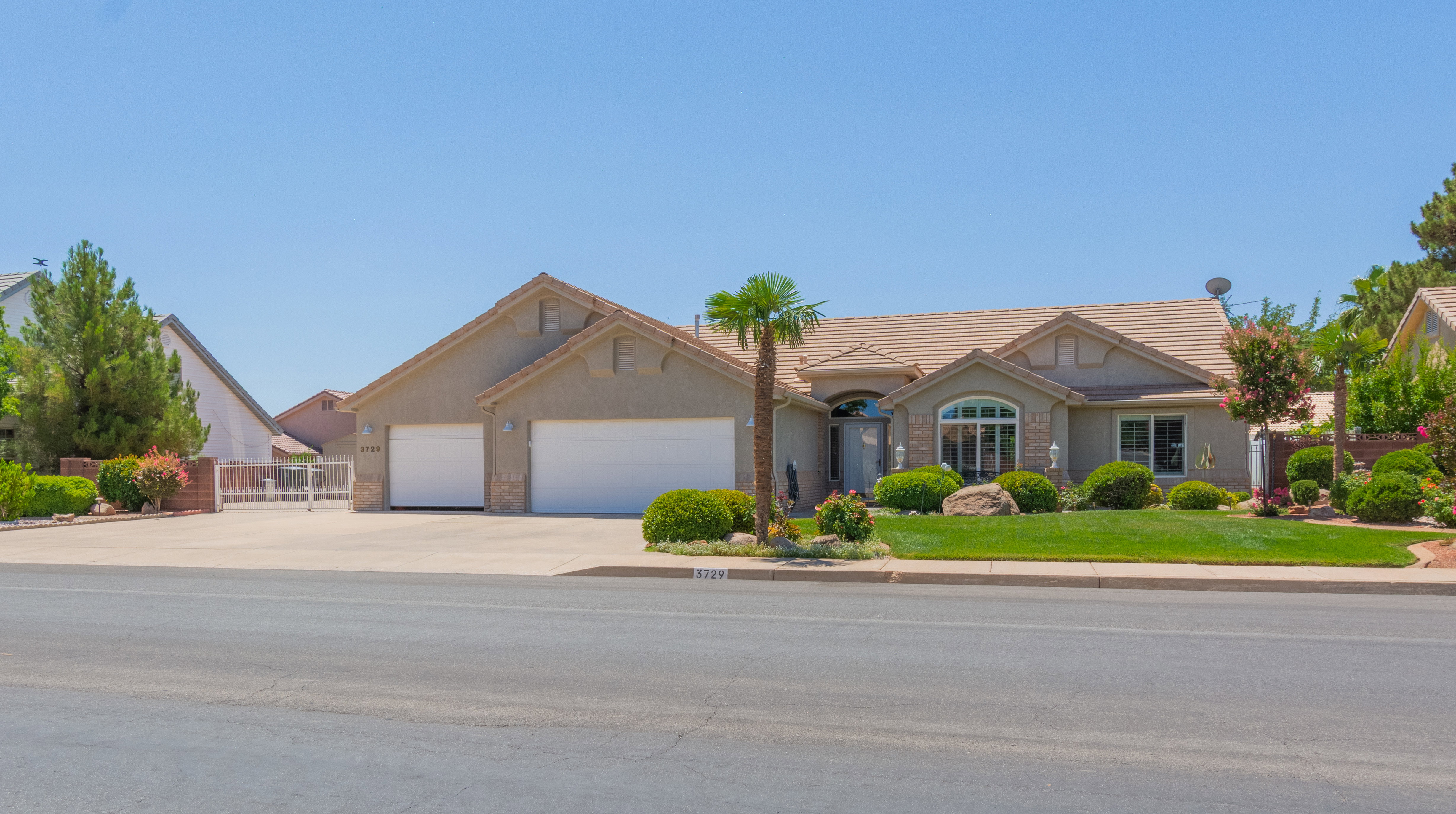 Stucco exterior with a tiled roof, two-car garage, manicured front lawn, mature landscaping, and an arched entry with a decorative front door