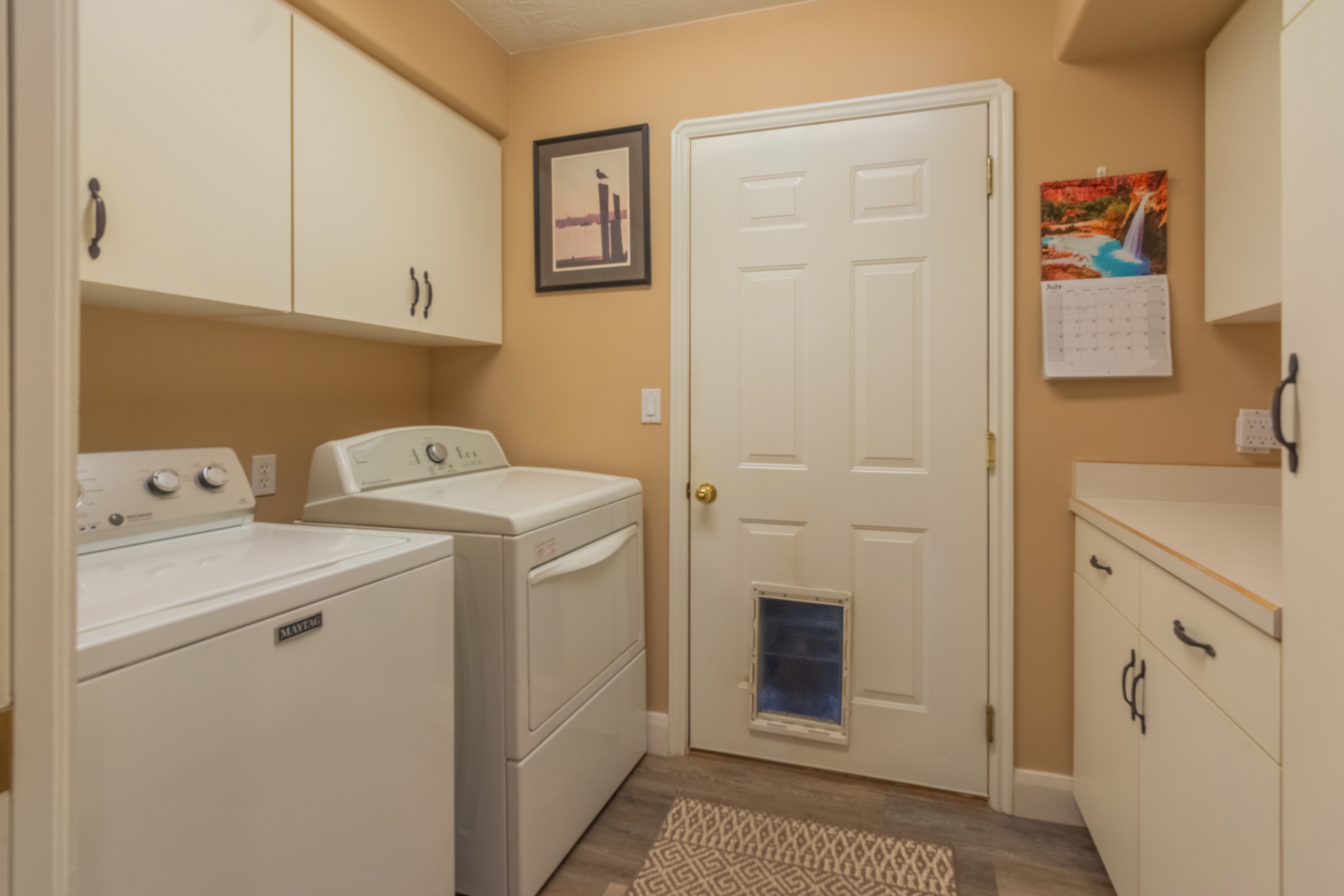 Laundry room featuring upper and lower cabinetry, ample countertop space, and wood-finish flooring