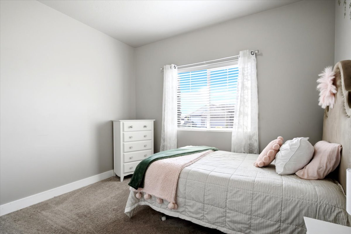 Bedroom featuring neutral-toned walls, a single window with white blinds and sheer curtains, and gray carpeting