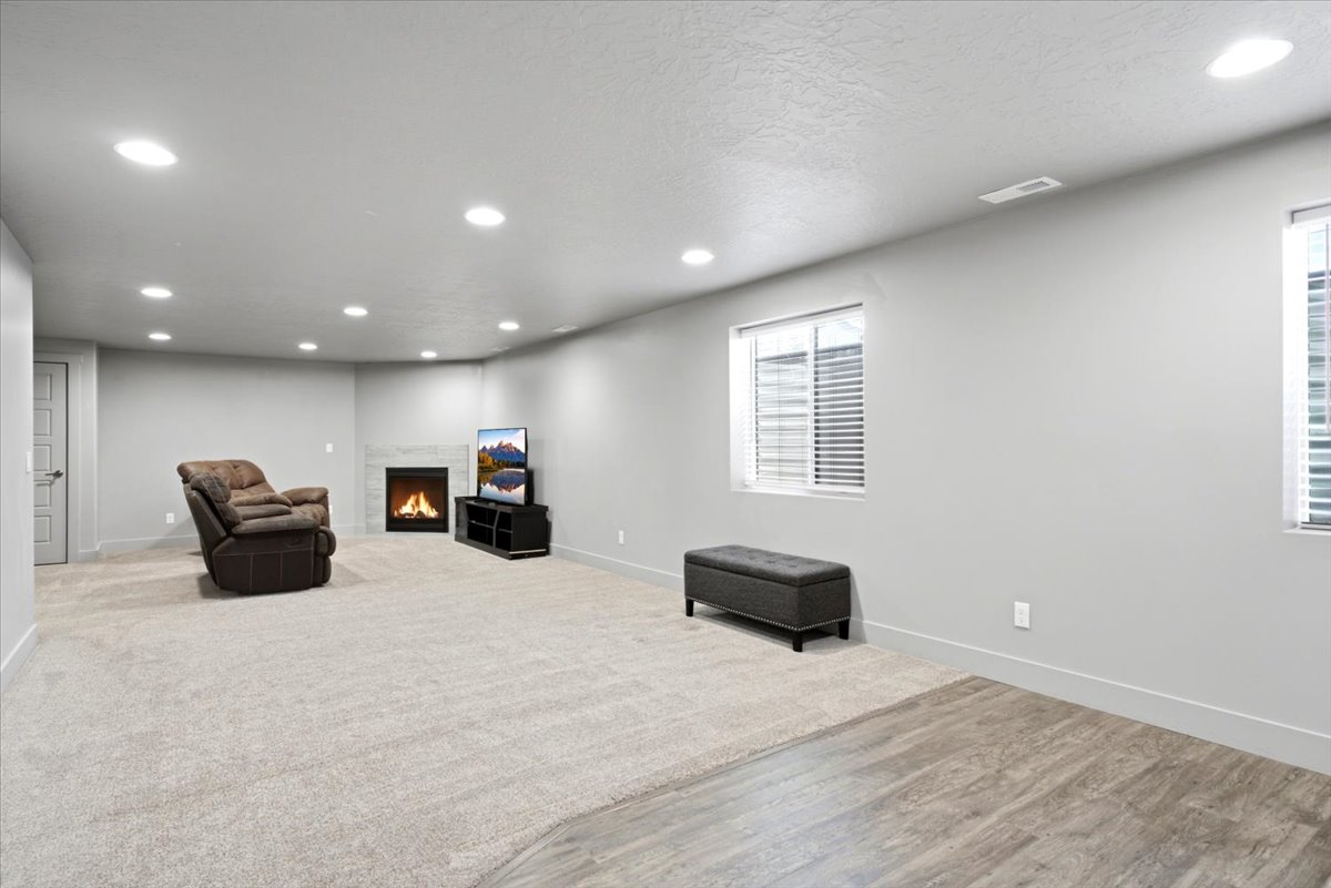 Spacious room featuring light-colored carpeting, recessed lighting, and a corner fireplace with a tiled surround