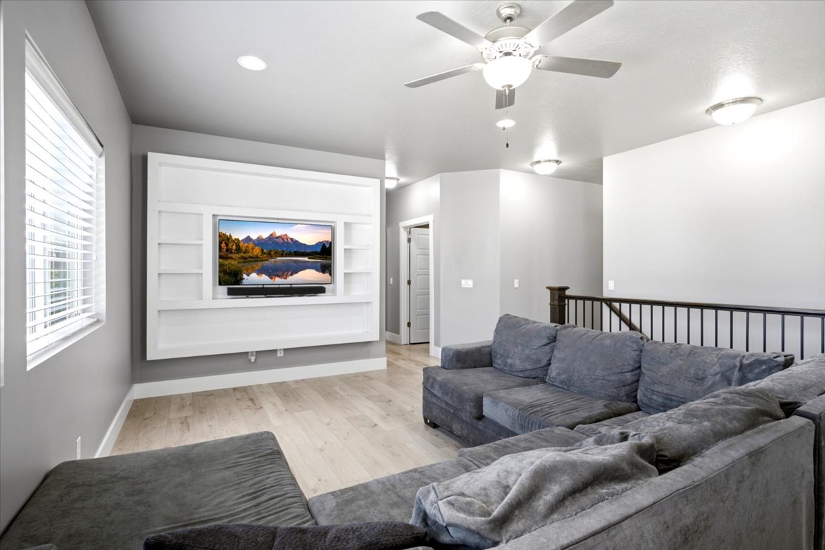 Living area featuring a custom white built-in media center with shelving, light wood-finish flooring, and a ceiling fan with integrated lighting