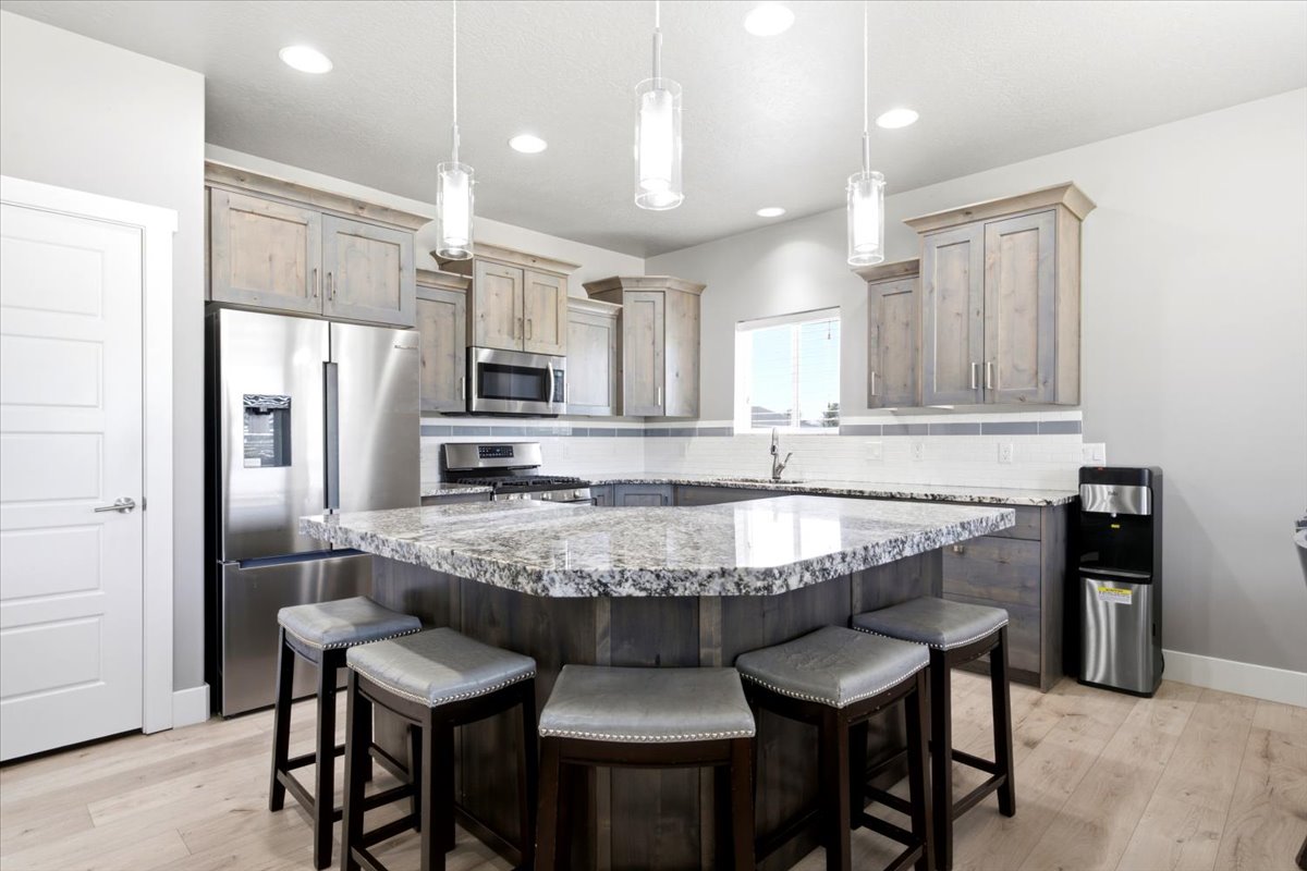 Gourmet kitchen featuring a large island with a speckled countertop, light wood-finish cabinetry, stainless steel appliances, and pendant lighting