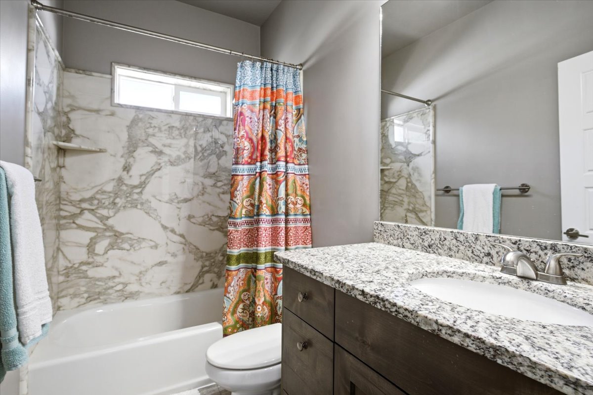 Bathroom featuring a white tub with marble-patterned surround, an integrated shelf, and an overhead window