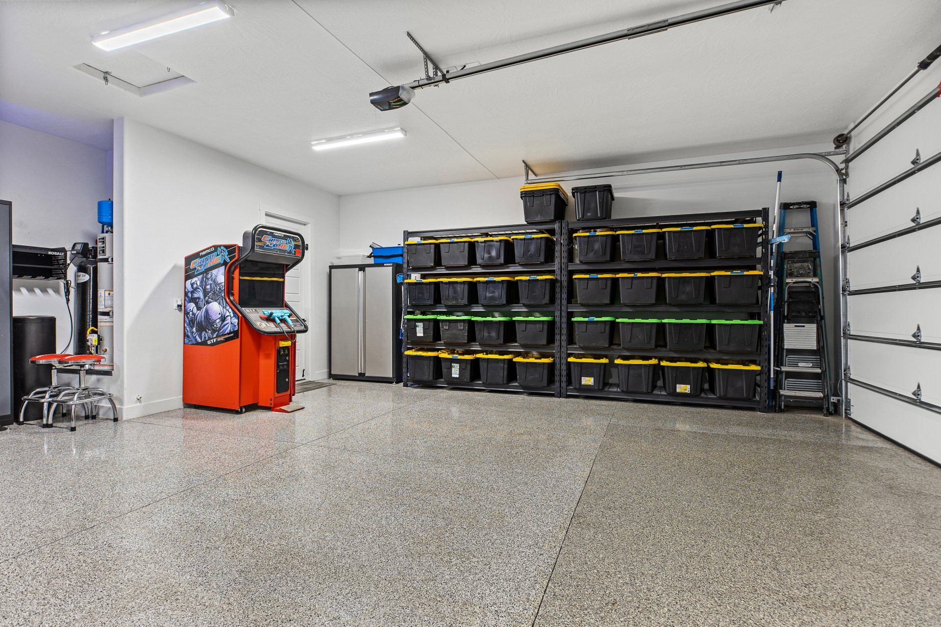 Expansive garage featuring a durable epoxy floor finish, overhead garage door, built-in storage shelving, and bright overhead lighting