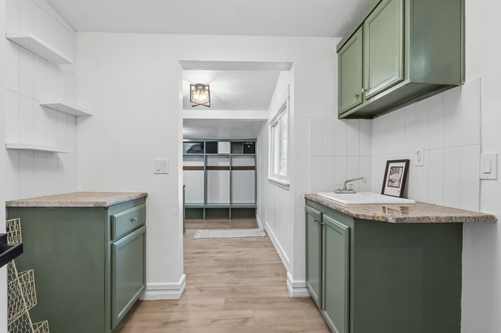 Kitchenette featuring sage green cabinetry, stone-look countertops, a built-in sink with faucet, white tiled backsplash, and wood-finish flooring