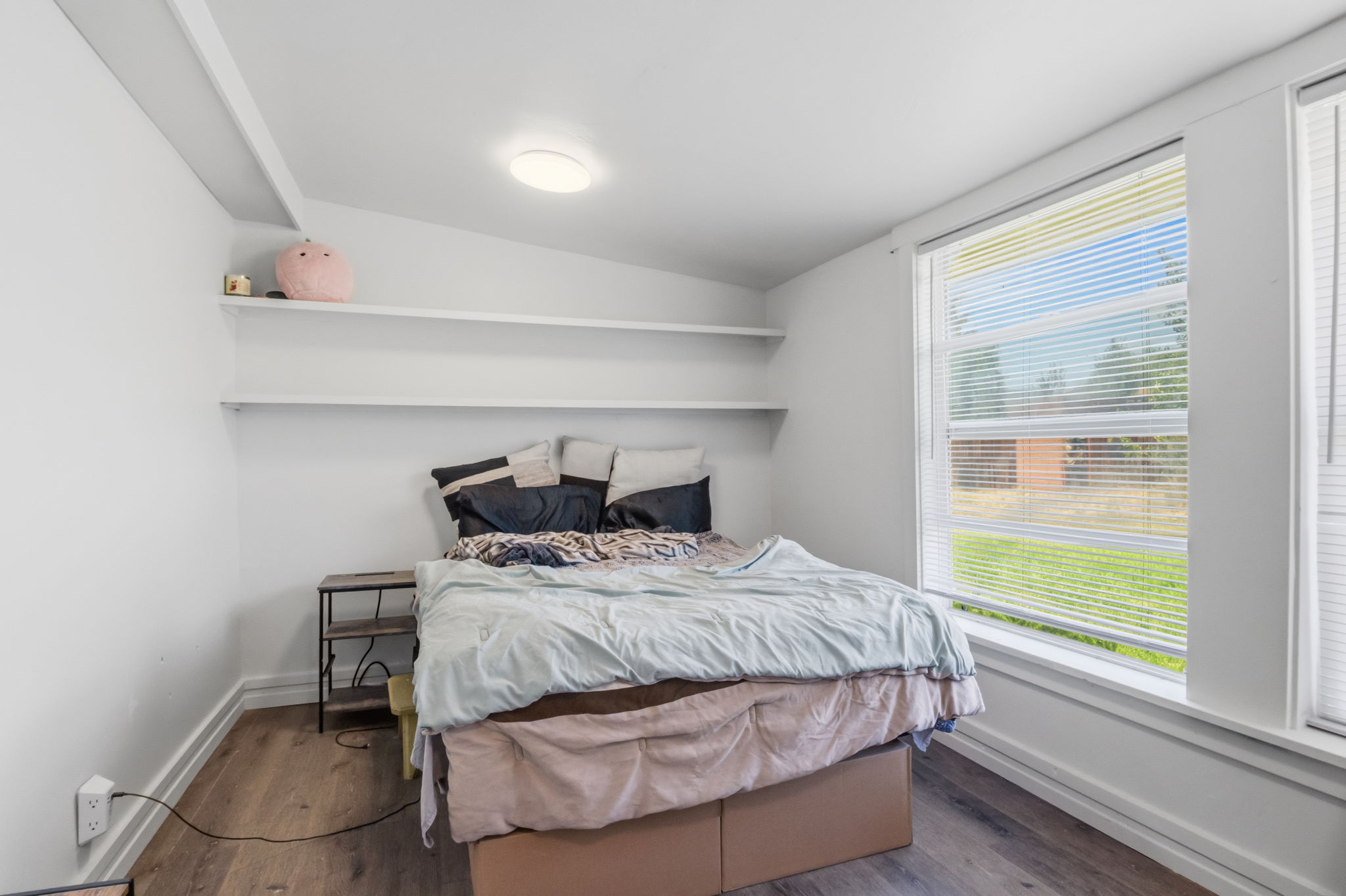 Compact room featuring wood-finish flooring, white walls, and a large window with horizontal blinds